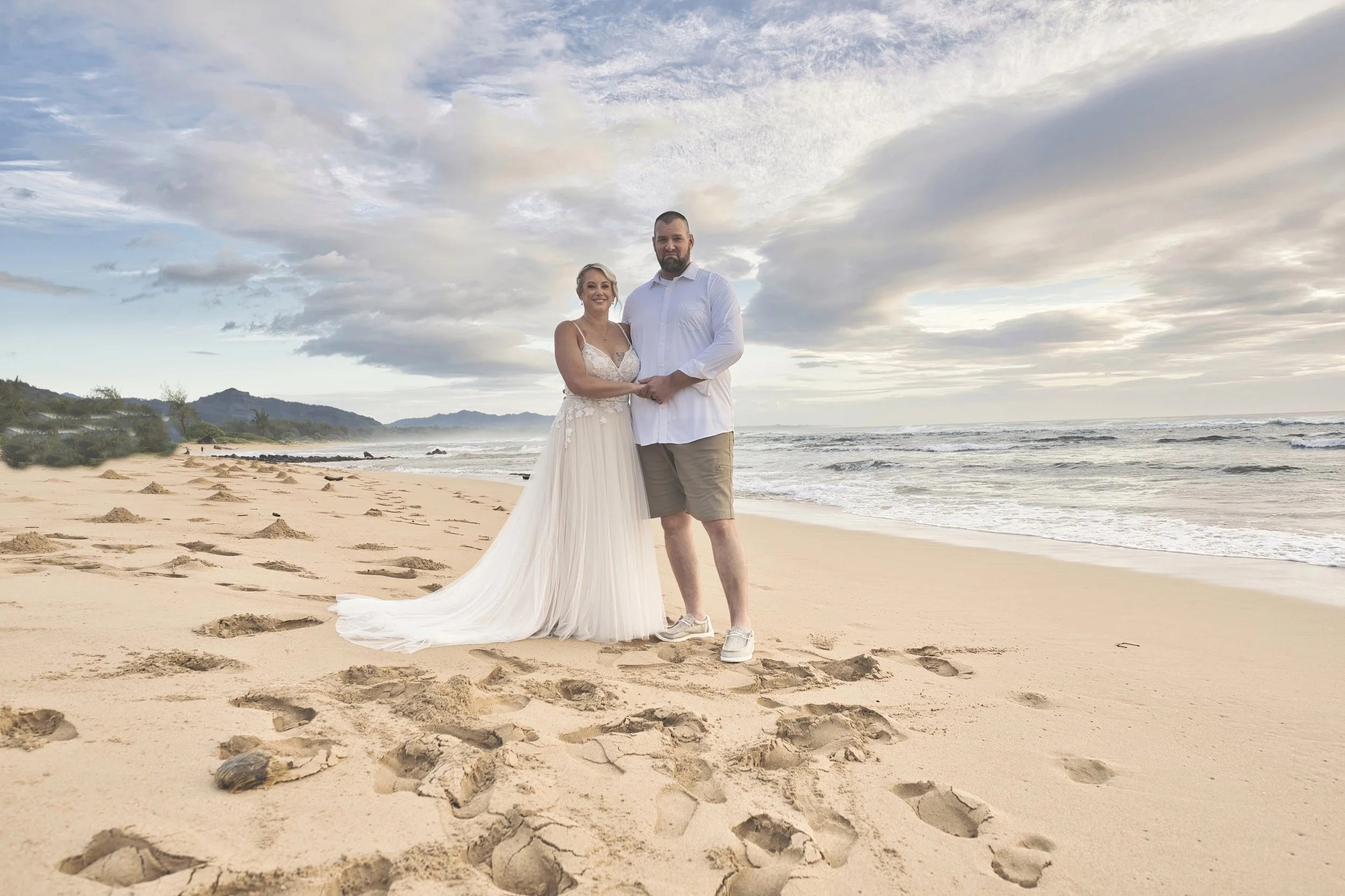 Newlywed couple posing on a Kauai beach surrounded by footprints in the sand.