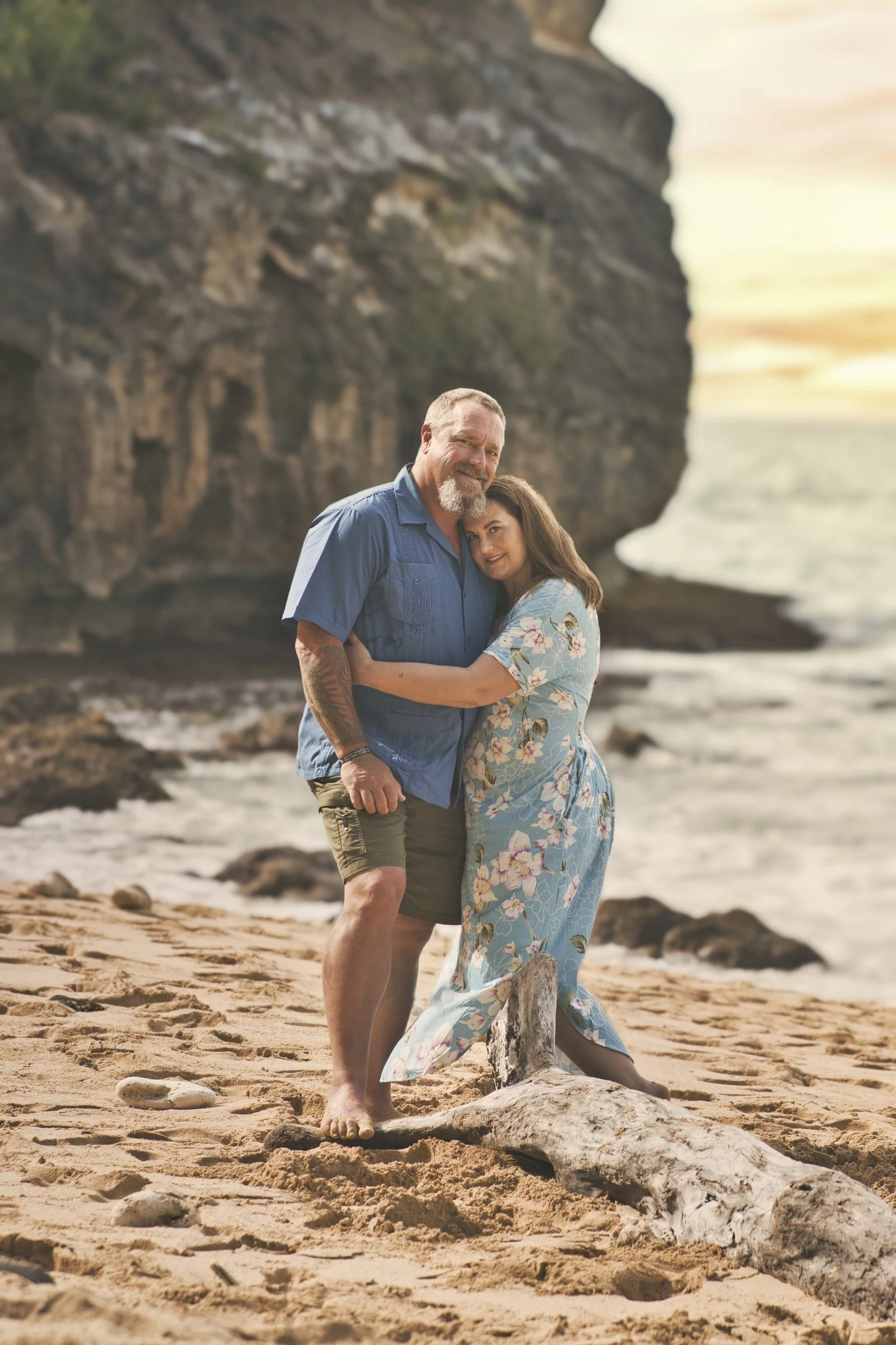 Couple embracing on the sandy beach beneath the cliffs at Shipwreck Beach, Kauai.