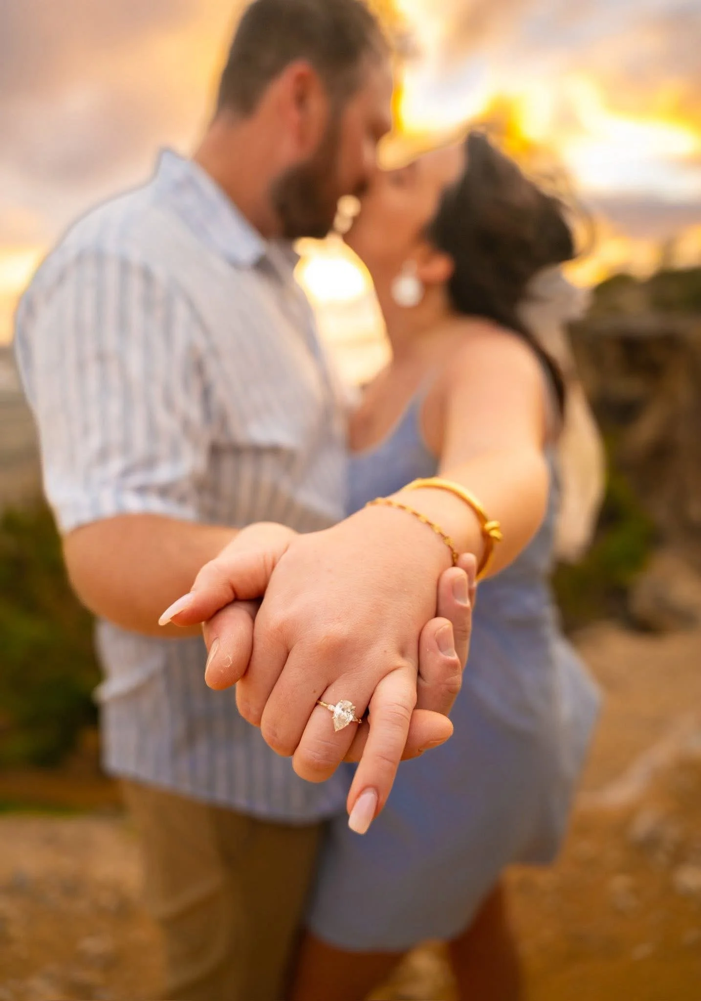 Couple kissing with joined hands extended to show the ring at Shipwreck Beach, Kauai.