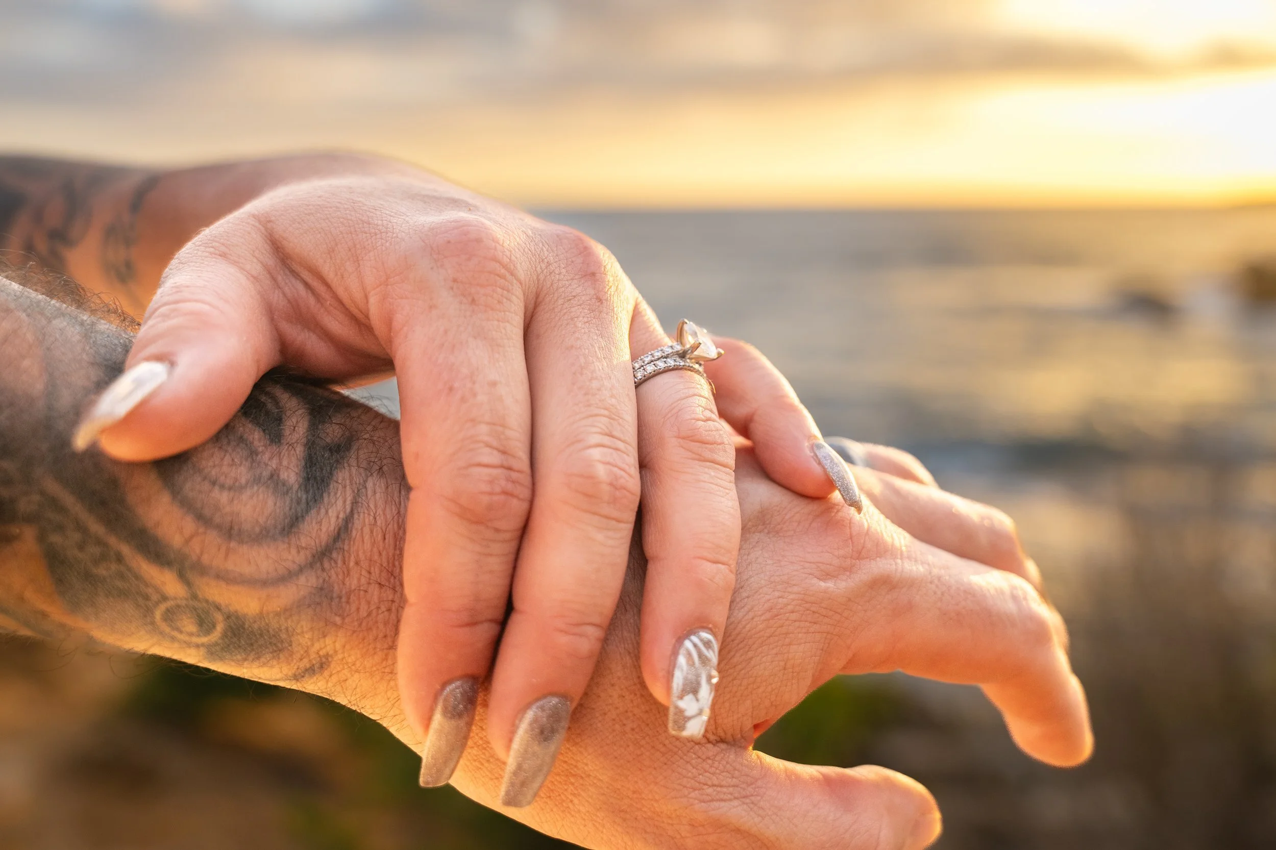 Close-up of wedding rings on a couple's hands with a Kauai sunset glowing behind them.