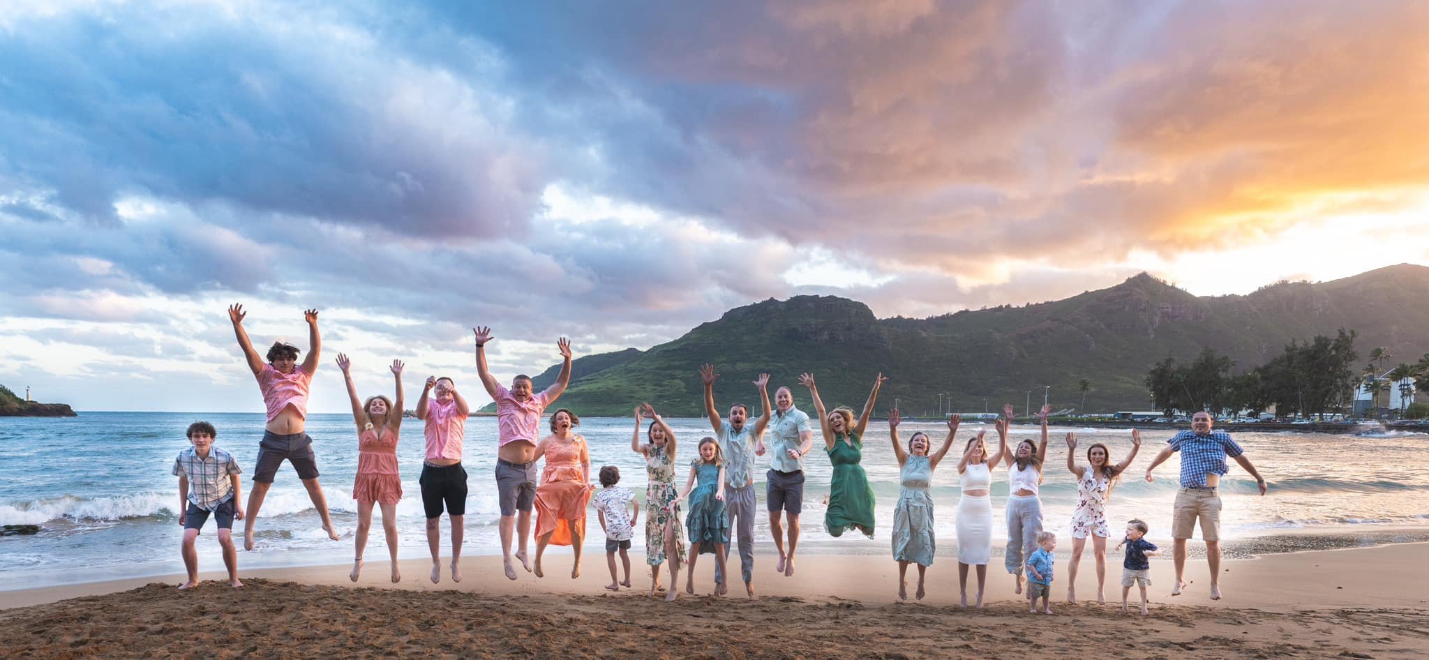 Large family jumping for joy on a Kauai beach at sunset with mountains in the background.