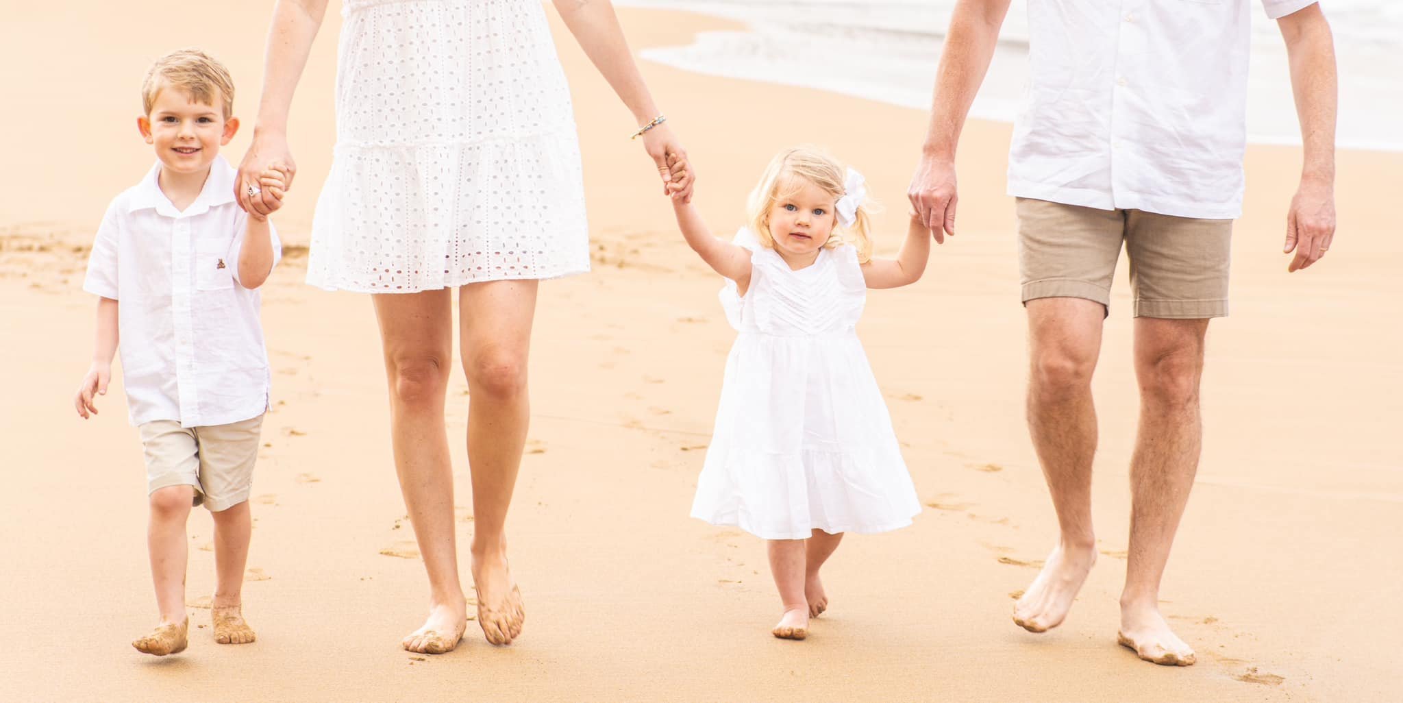 Parents walk hand-in-hand with their young son and daughter along a sandy Kauai beach.