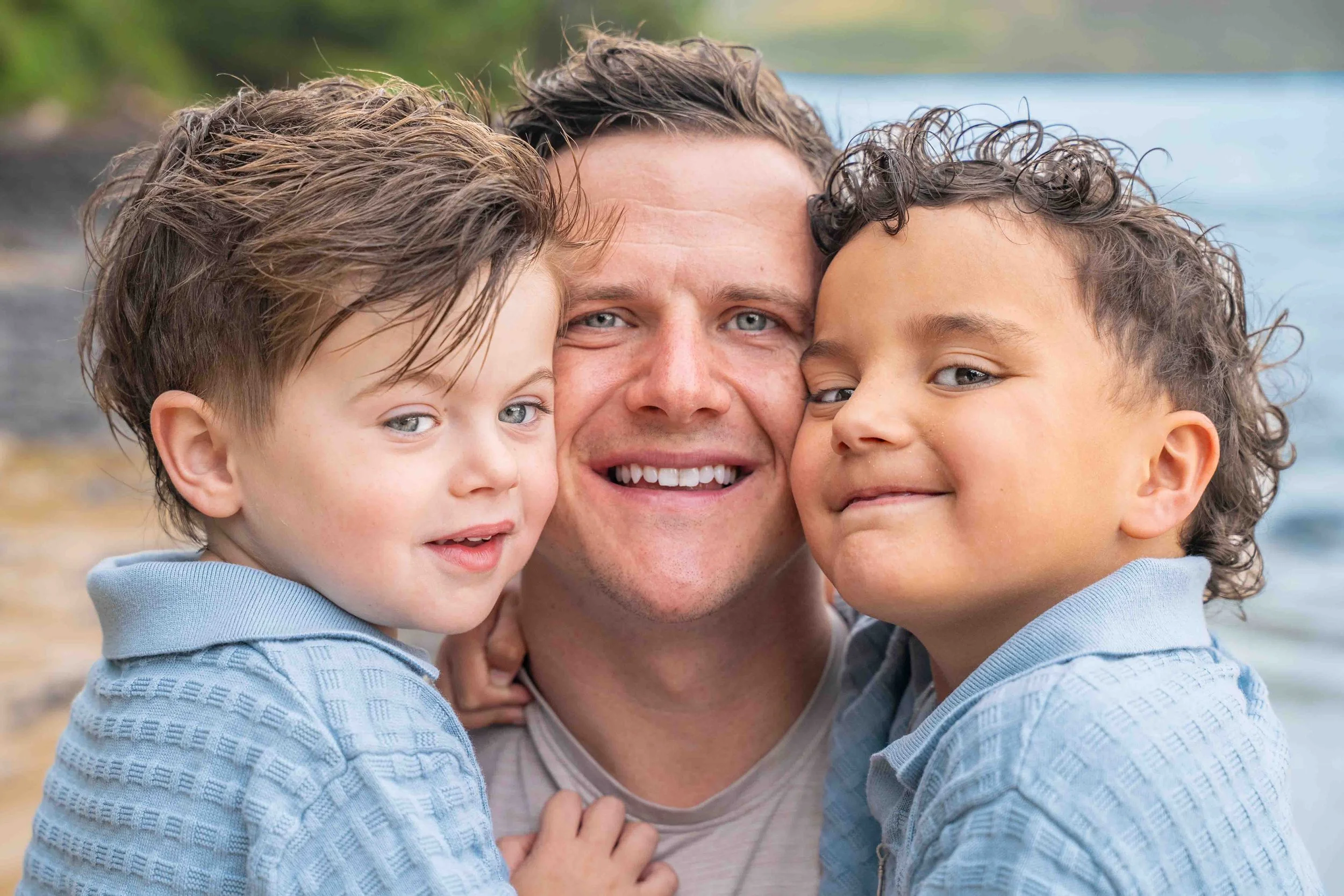 Smiling dad with his two young sons pressed against him on a Kauai beach.