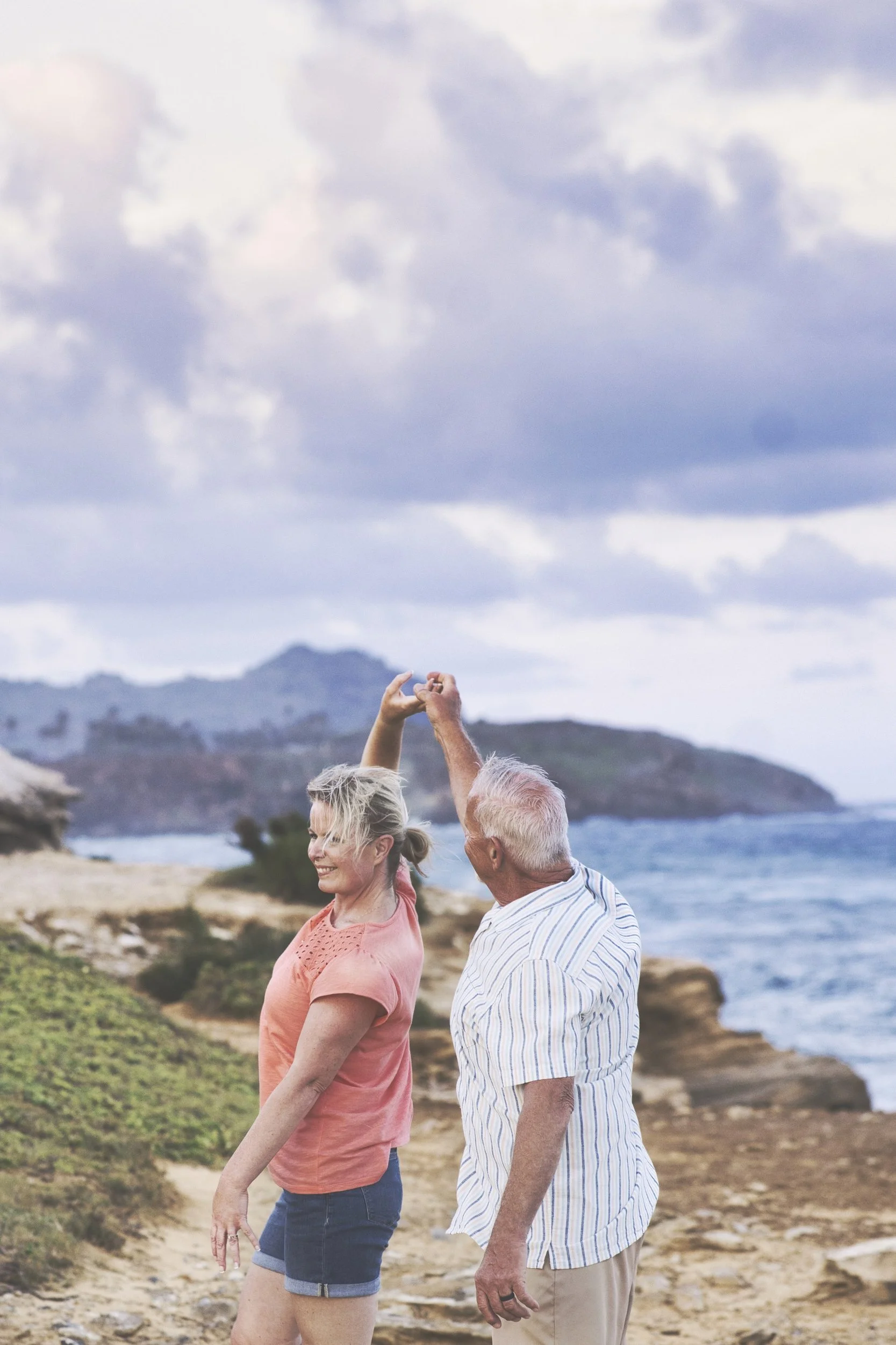Senior couple strolling hand in hand on a cliff path at Shipwreck Beach, Kauai.