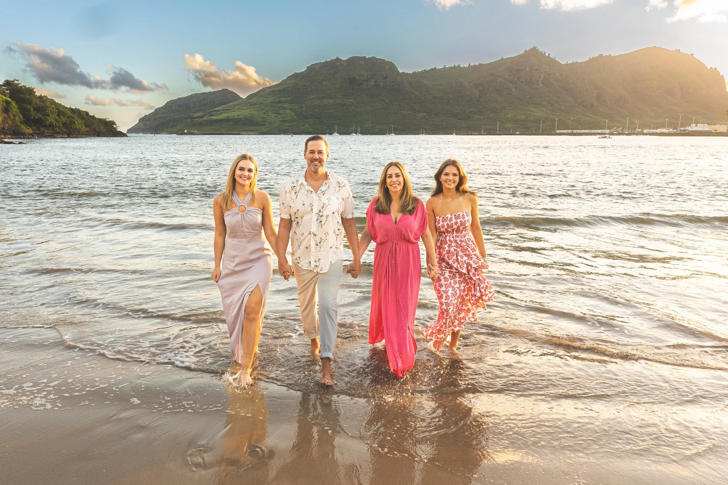 Family of four wading through shallow water toward the camera on Kauai at sunset.