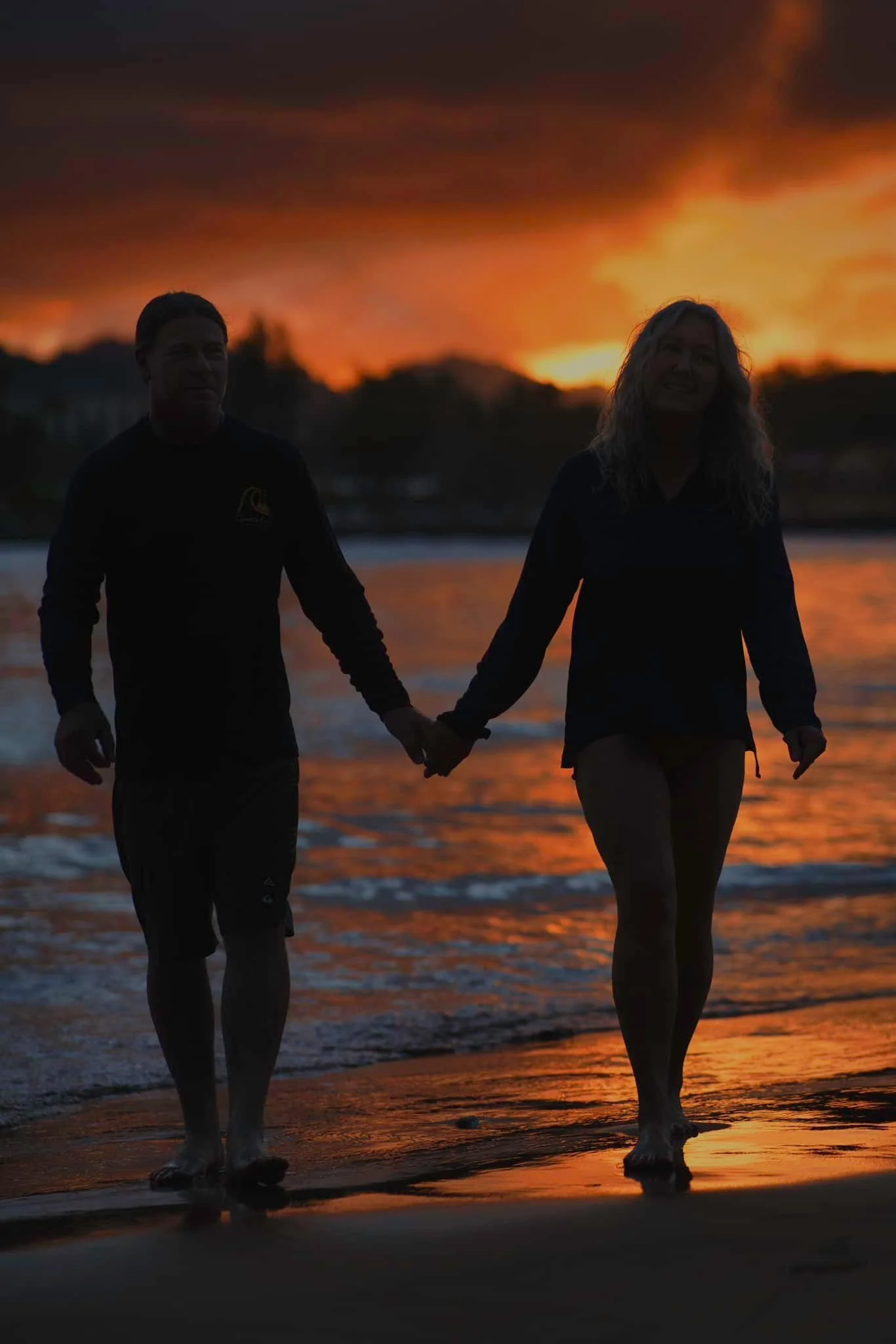 Couple's silhouettes holding hands under a glowing sunset on a Kauai beach.