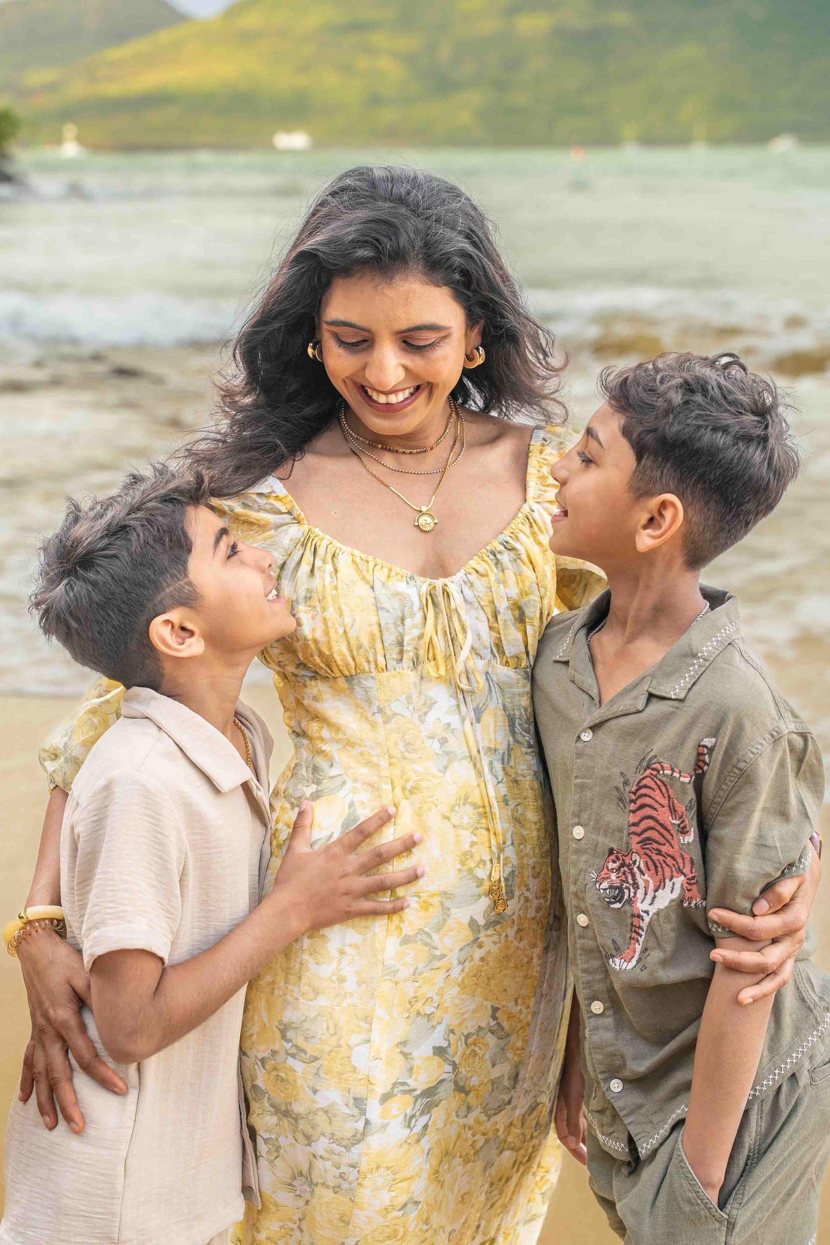 Mom in a yellow floral dress smiling with her two sons on a Kauai beach.