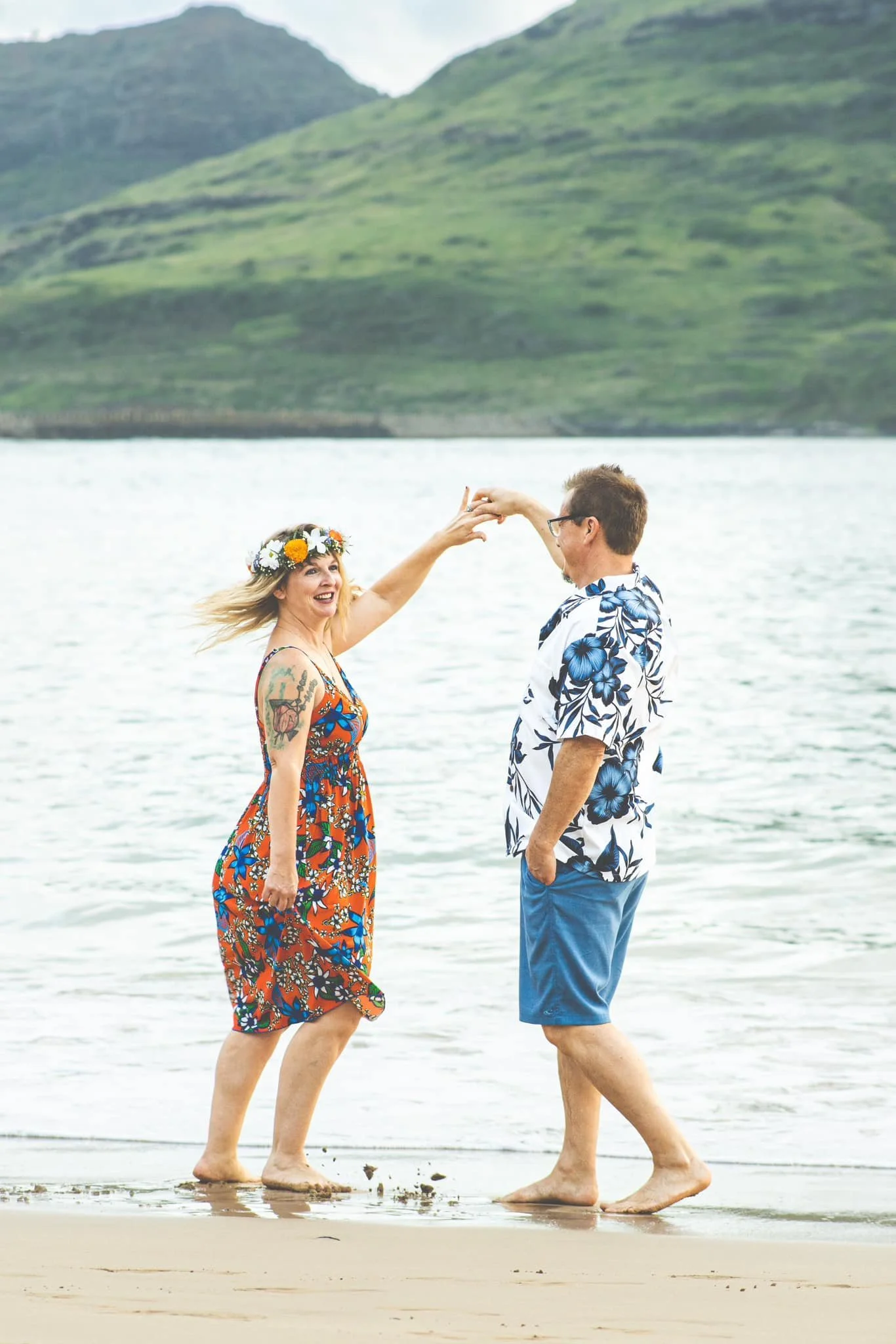 Woman in a flower crown twirling while dancing with her partner on a Kauai beach.