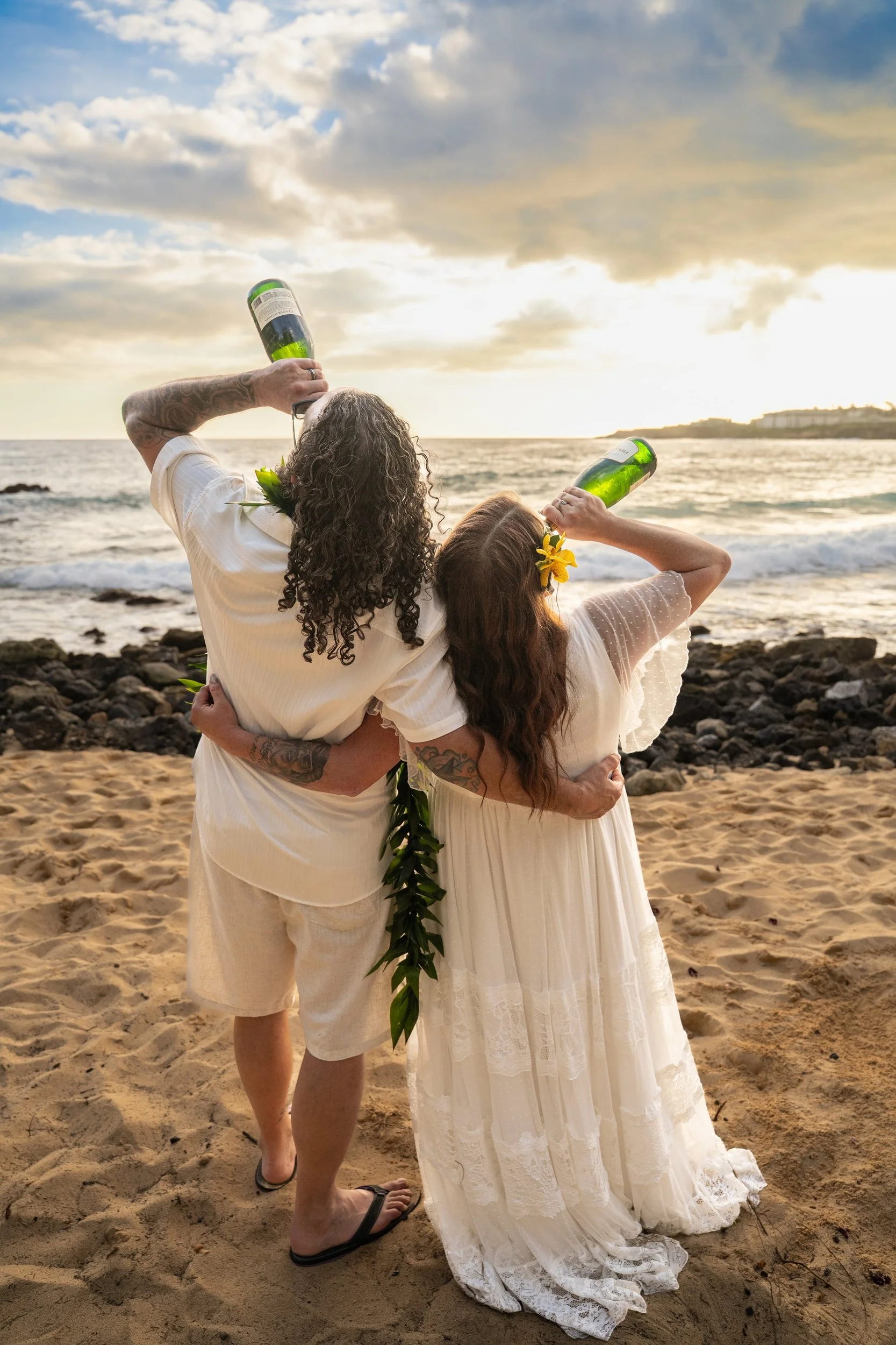 Newlywed couple toasting with champagne on a Kauai beach at sunset.