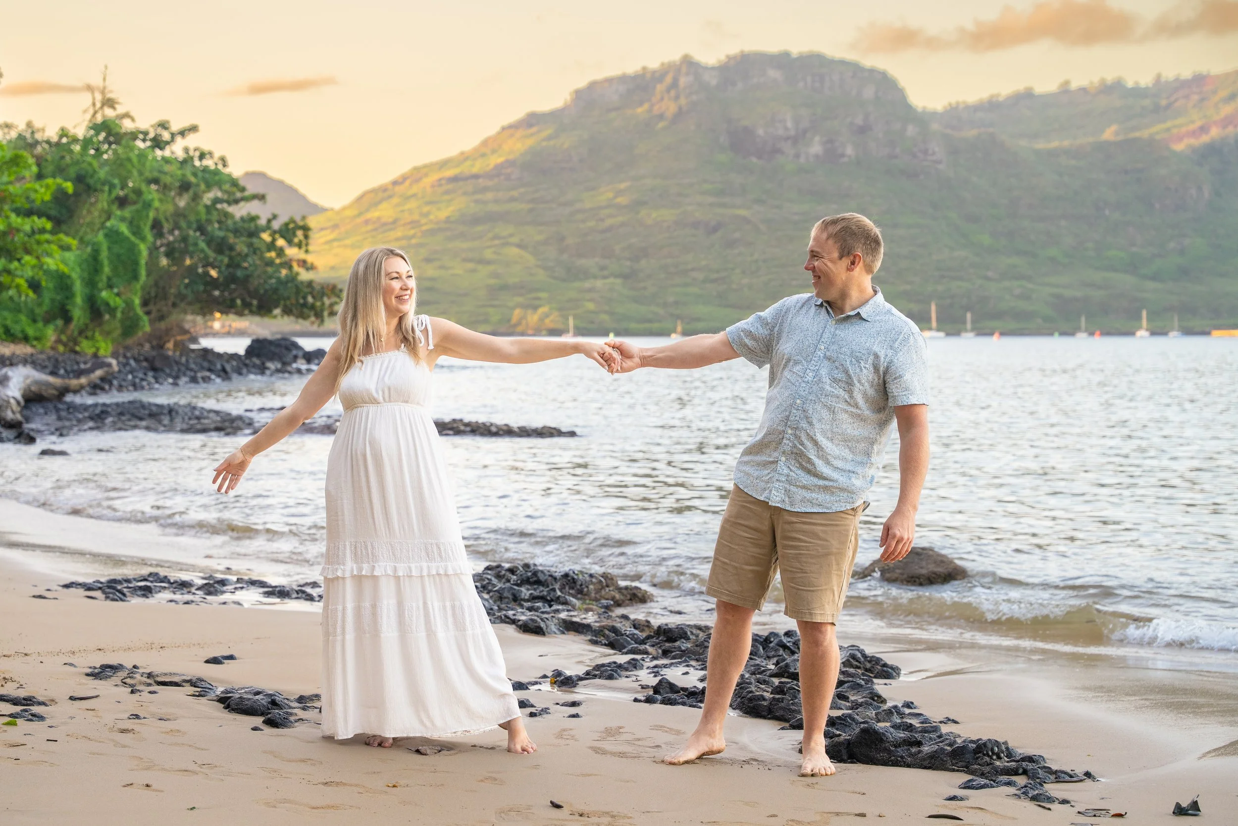 Couple holding hands and smiling on a Kauai beach at sunset.