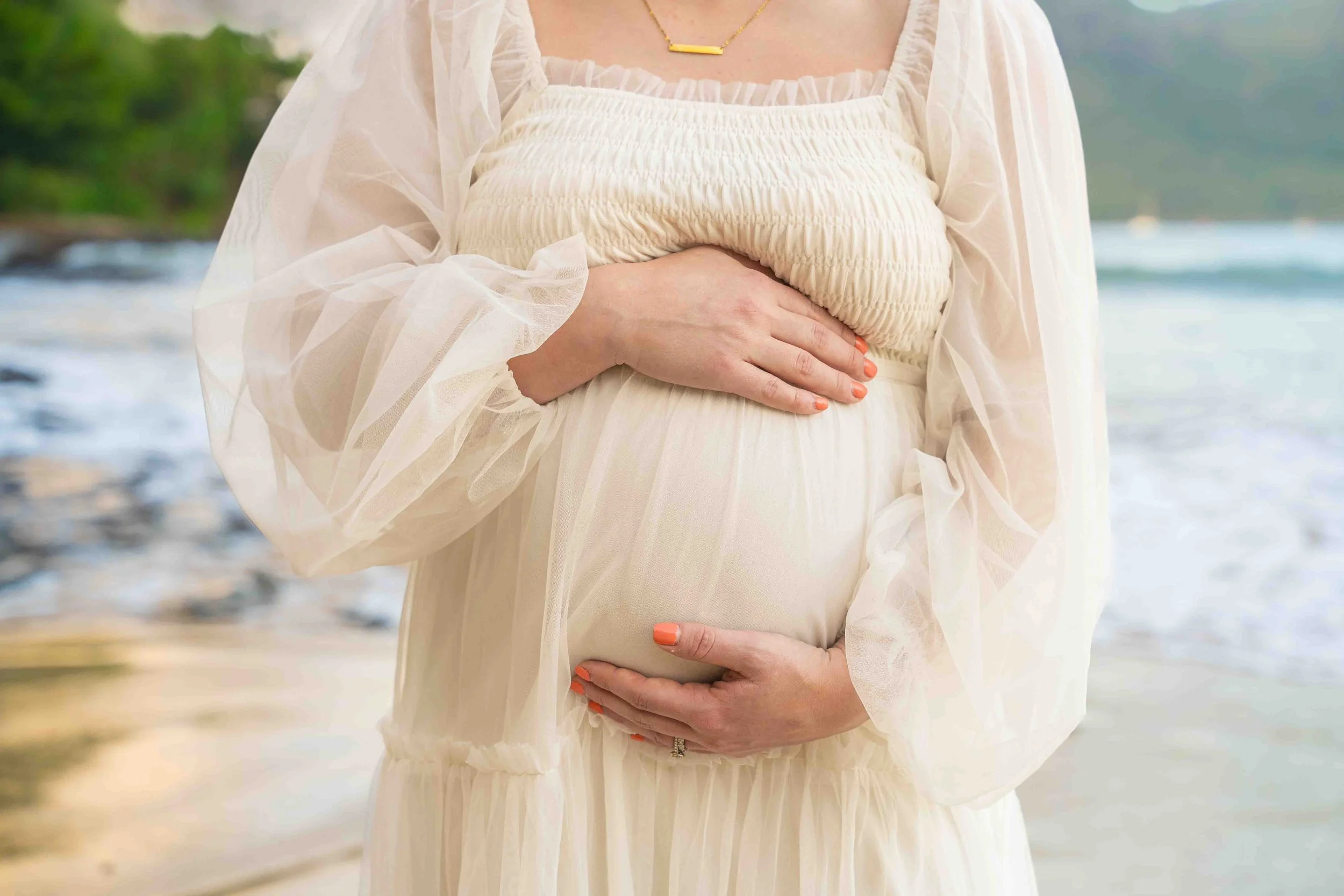 Close-up of an expecting mom cradling her baby bump on a Kauai beach.