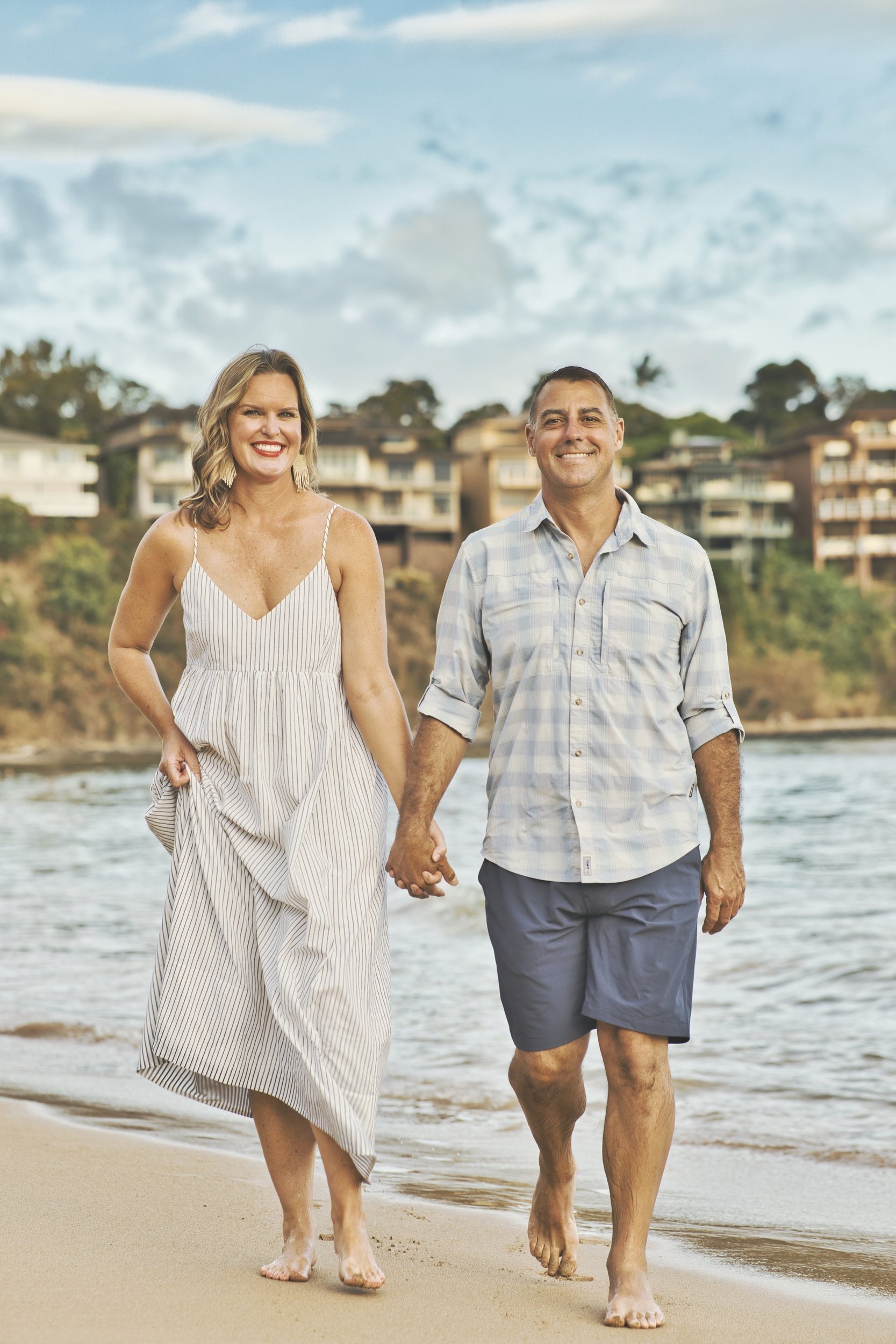 Smiling couple walking hand in hand toward the camera on a Kauai beach.