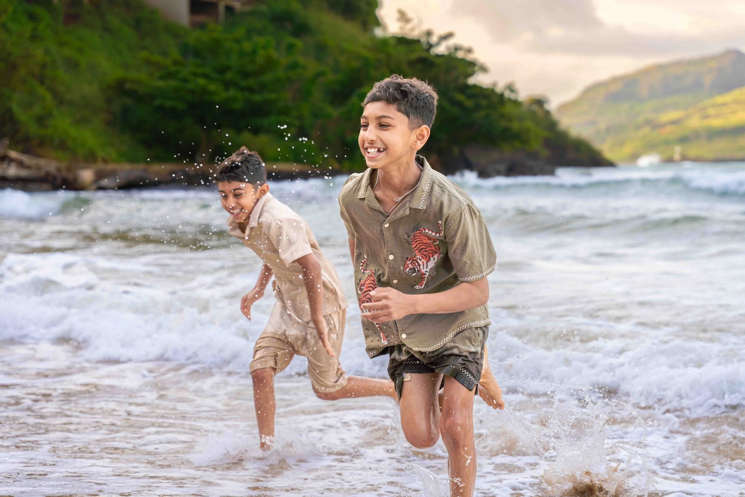 Two brothers laughing while running through the ocean surf on a Kauai beach.