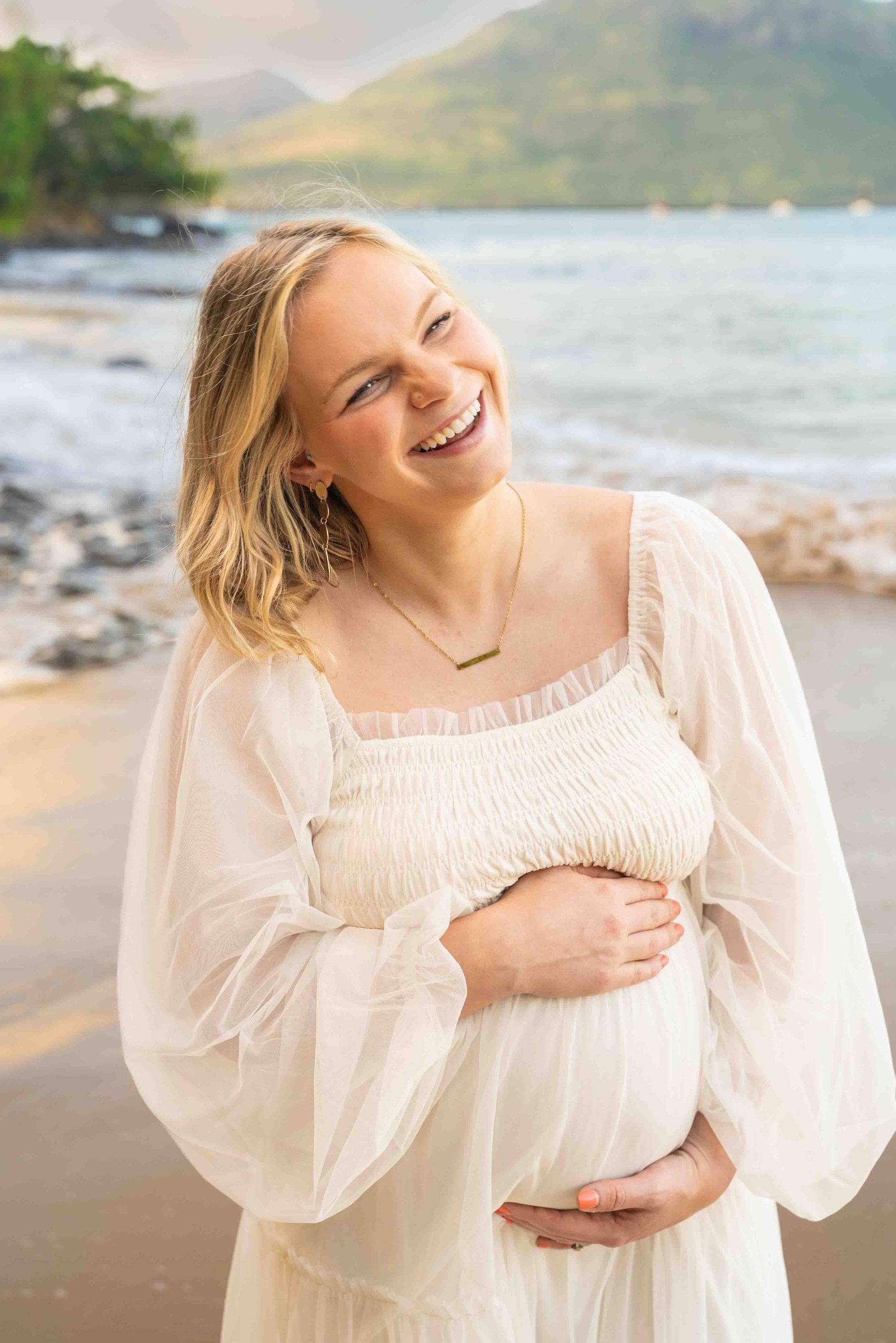 Smiling expecting mom cradling her belly on a Kauai beach.
