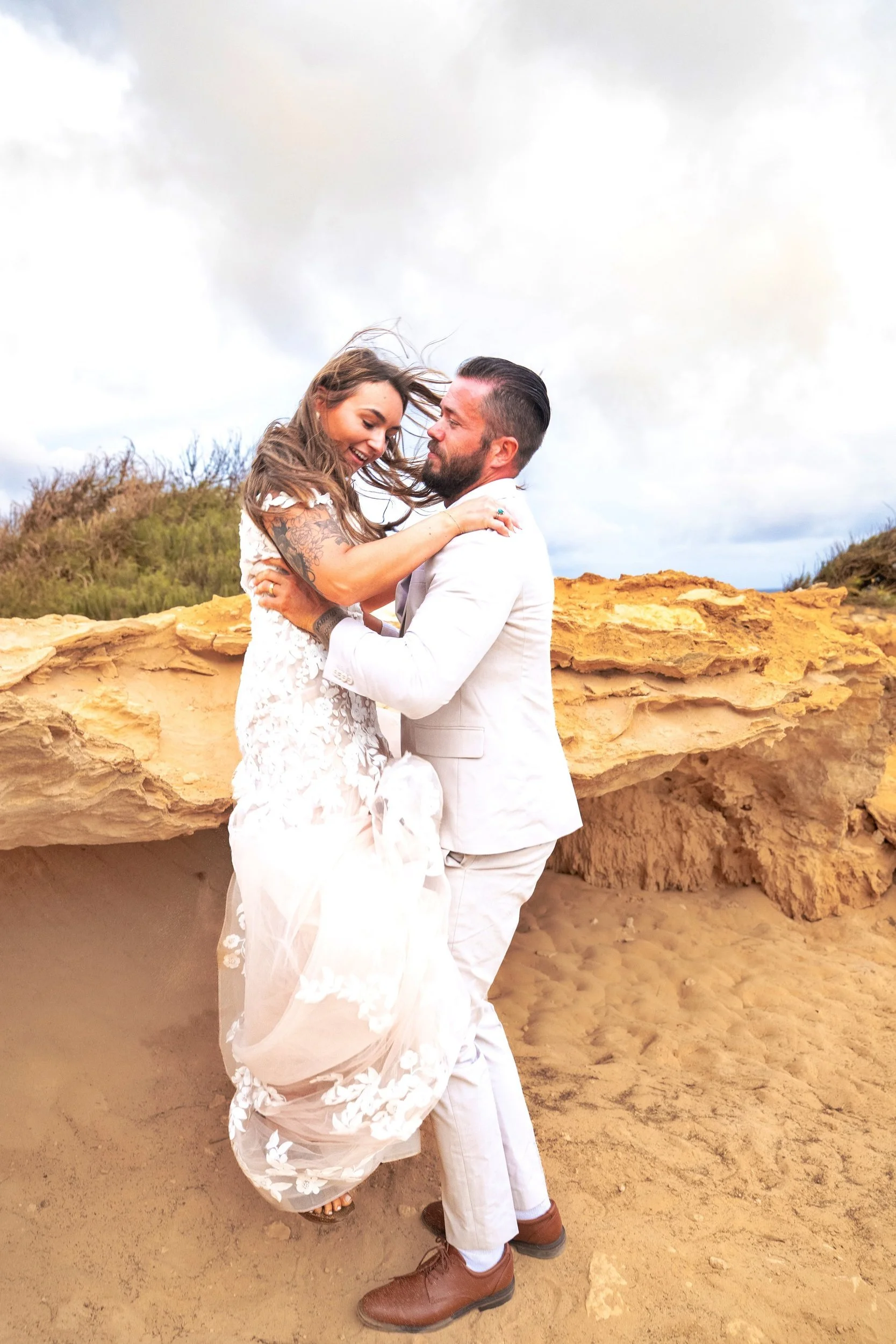 Groom playfully lifting his laughing bride on the cliffs at Shipwreck Beach, Kauai.