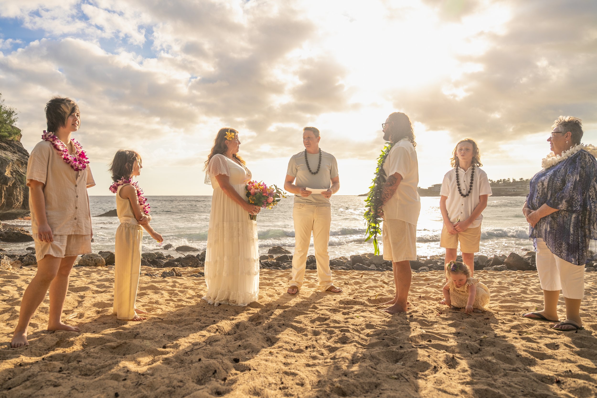 Intimate beach wedding ceremony with family on the sand in Kauai at sunset.