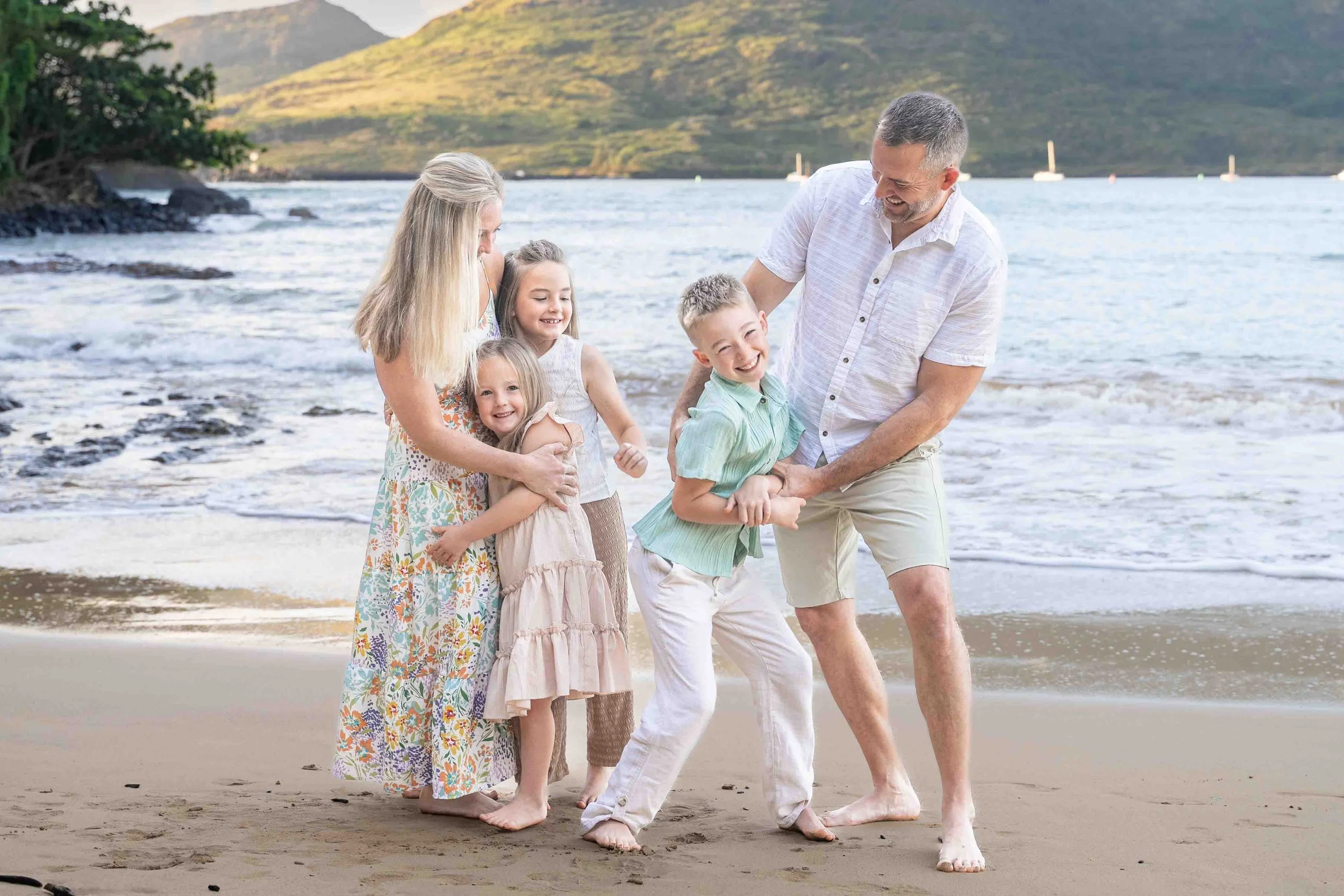 Family of five laughing together on a Kauai beach at the water's edge.