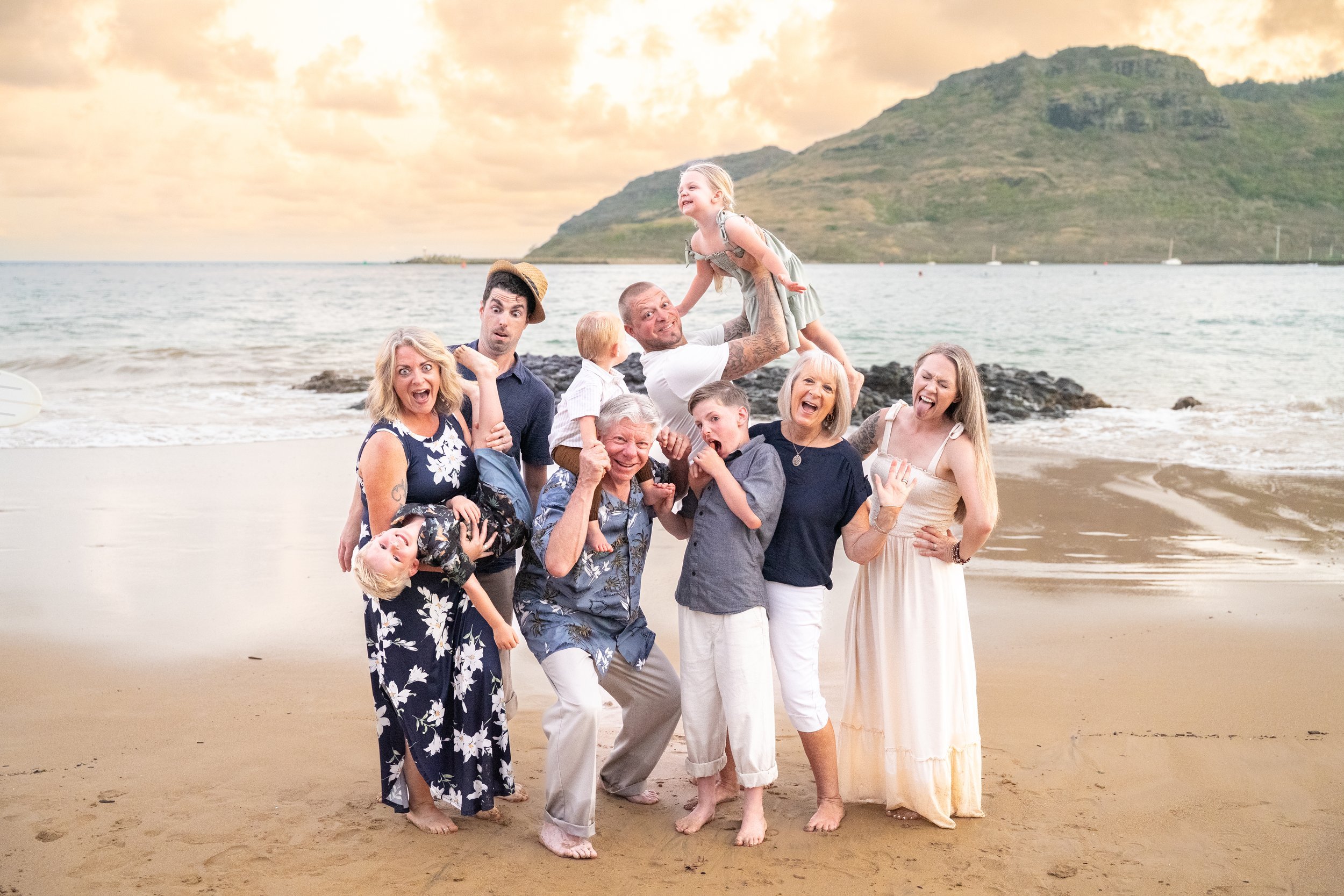 Large family making silly faces and goofy poses on a Kauai beach at sunset.