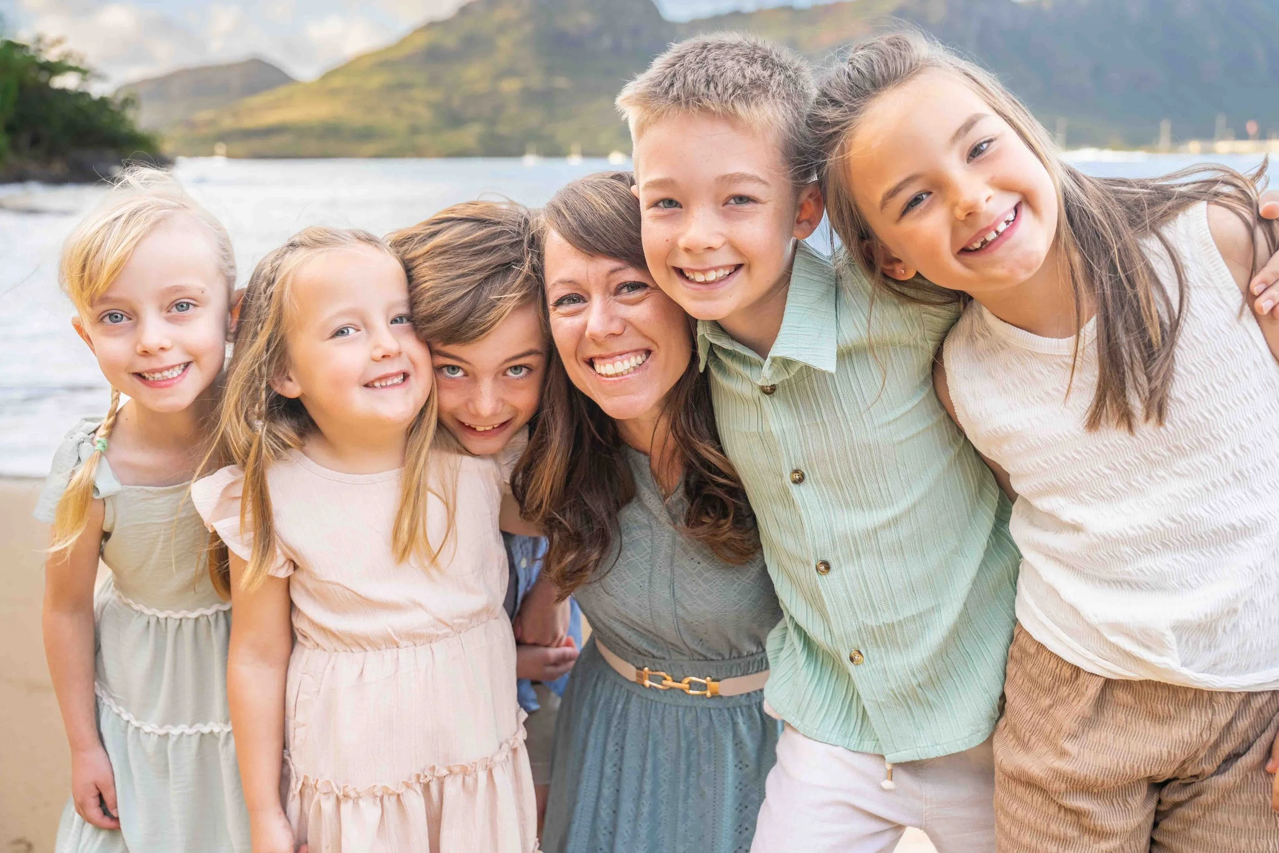 Mom huddled close with her five kids smiling on a Kauai beach.
