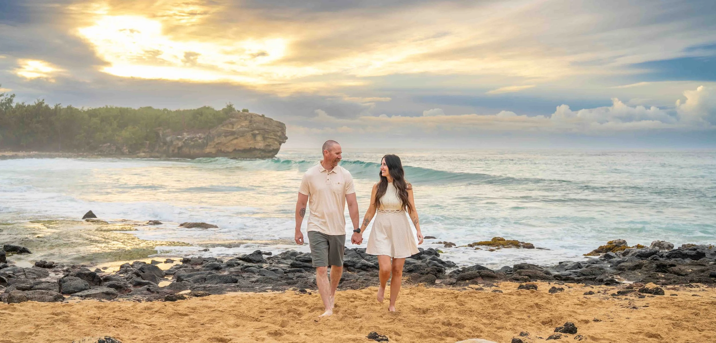 Couple holding hands strolling along the beach at Shipwreck Beach, Kauai.