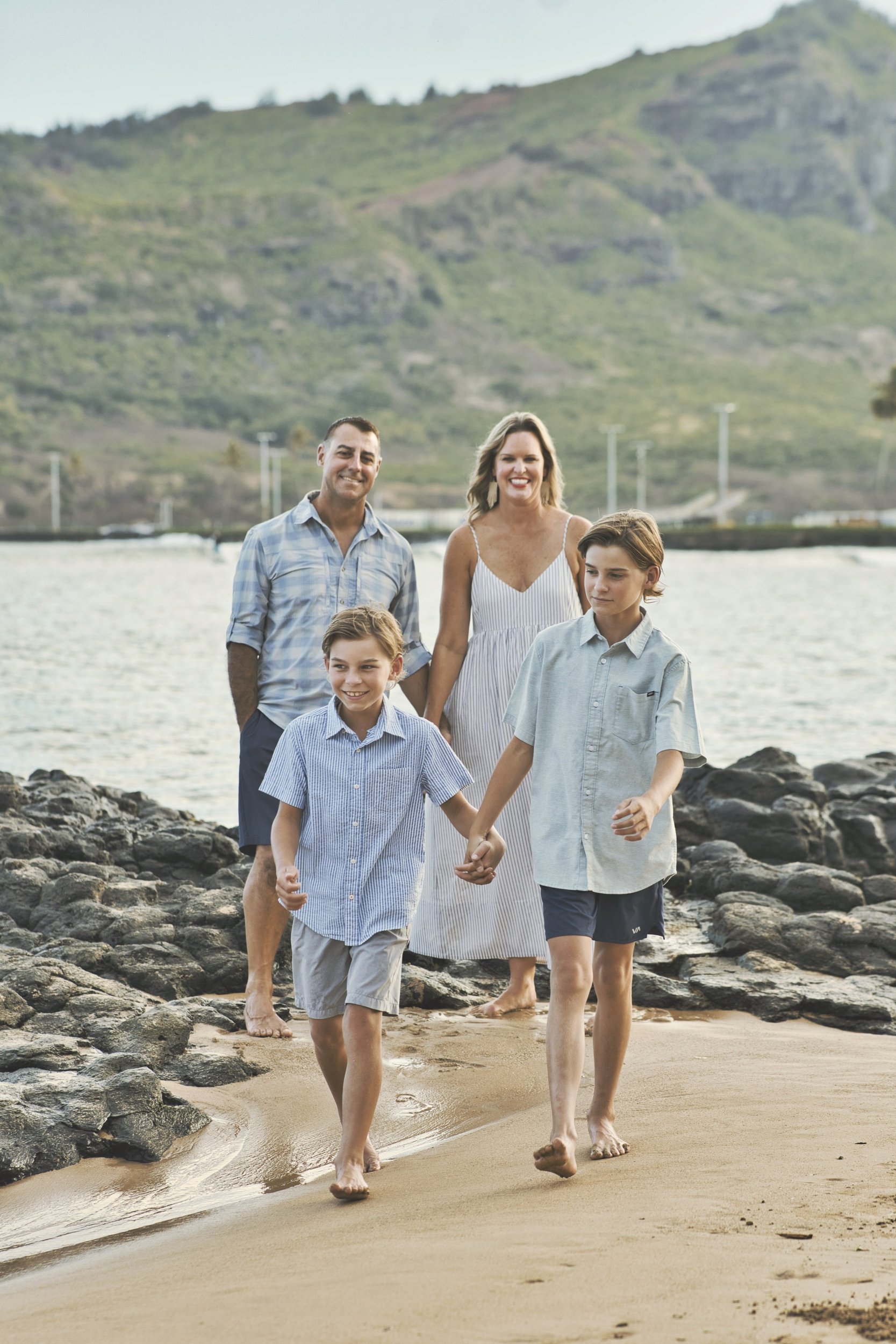 Family of four walking along a Kauai beach, the two boys leading hand in hand.