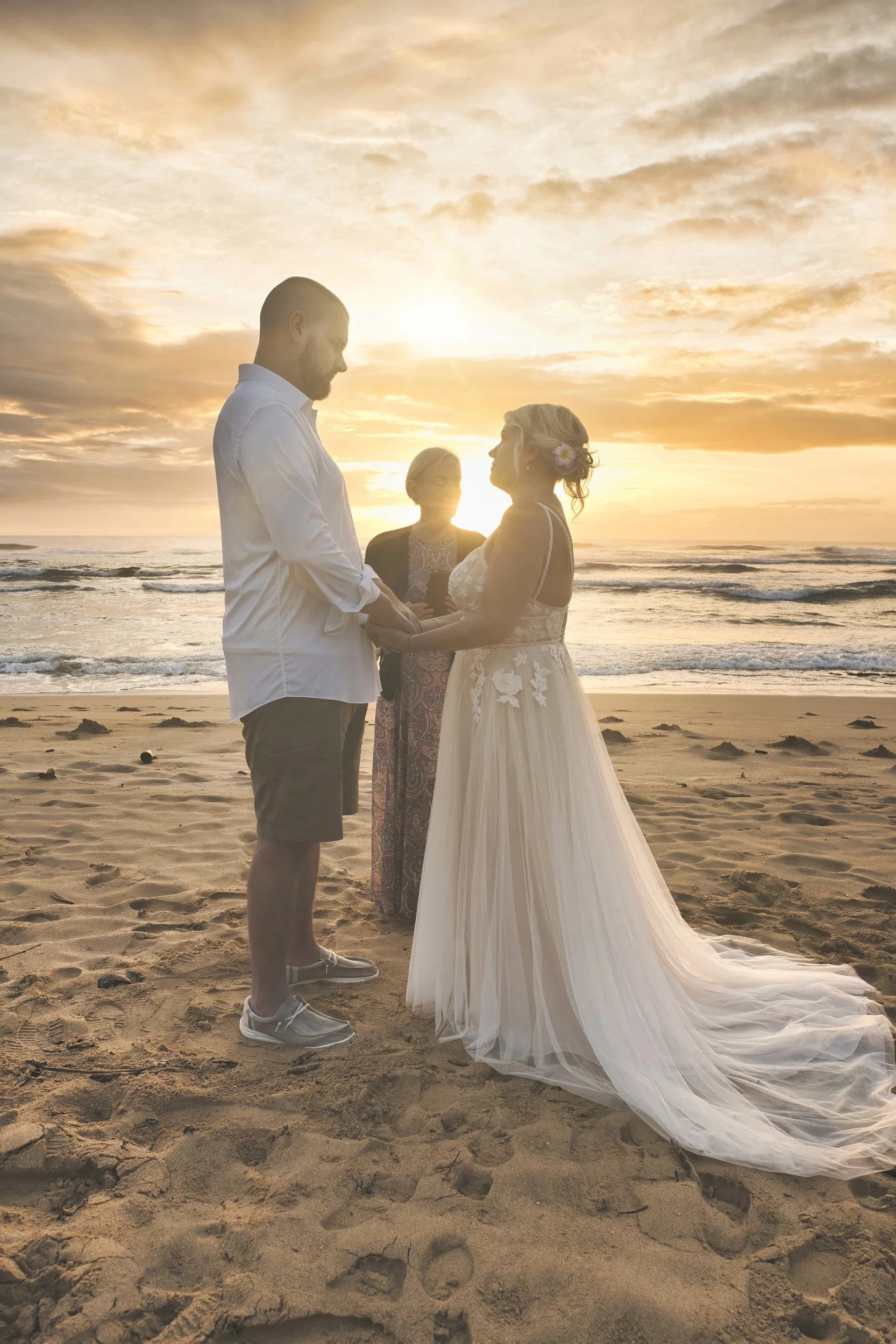 Newlywed couple exchanging vows on a Kauai beach silhouetted against a golden sunset.