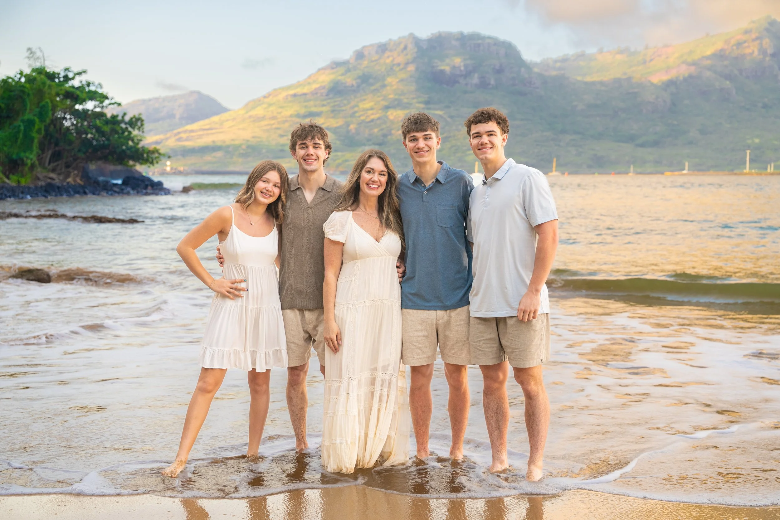 Family with three teenage boys standing in the surf on a Kauai beach.