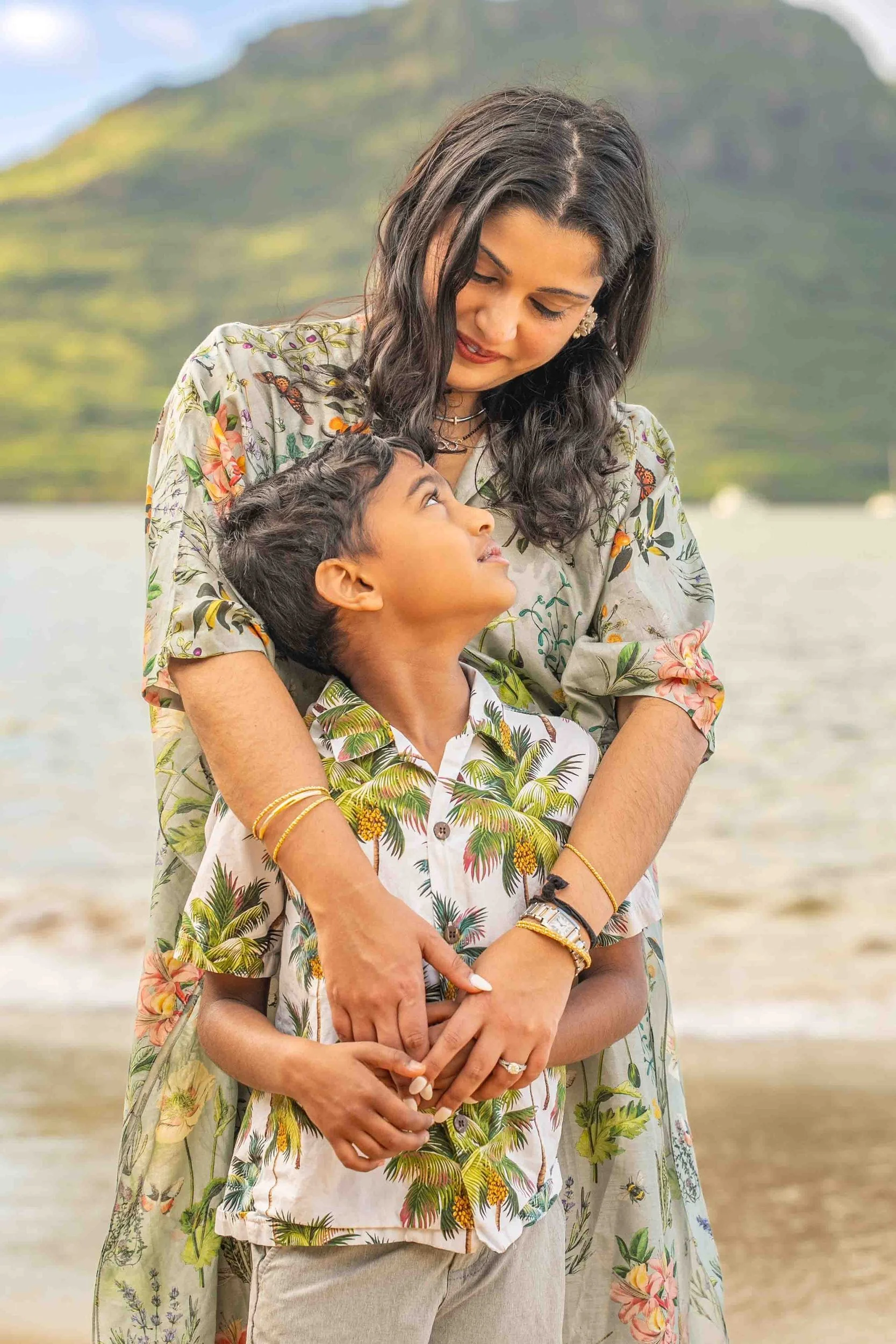 Mom hugging her son and looking down at him on a Kauai beach.