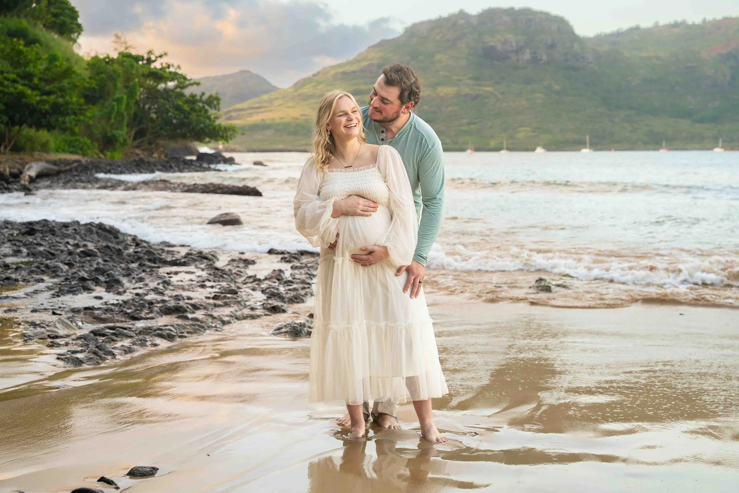 Expecting couple cradling the baby bump on a Kauai beach.