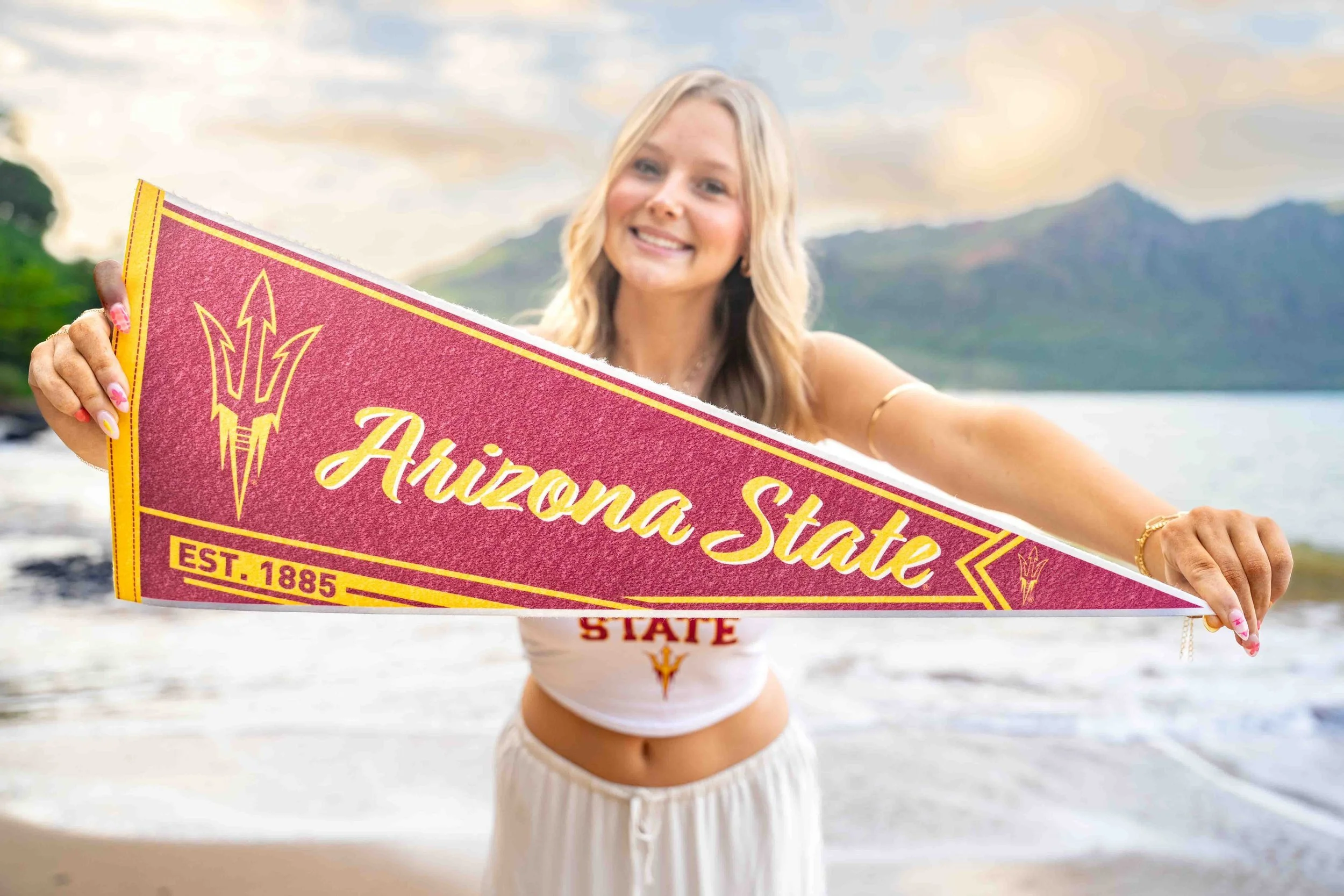 Young woman holding an Arizona State pennant on a Kauai beach.