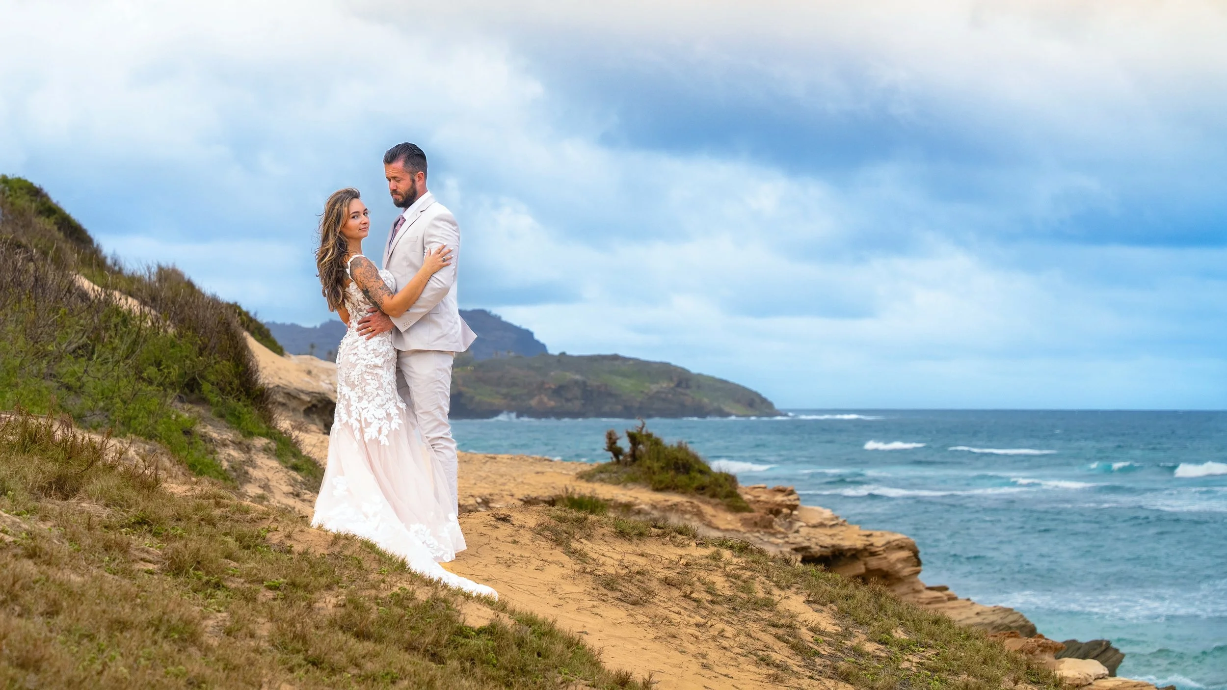 Newlywed couple embracing on a cliff path above the ocean at Shipwreck Beach, Kauai.