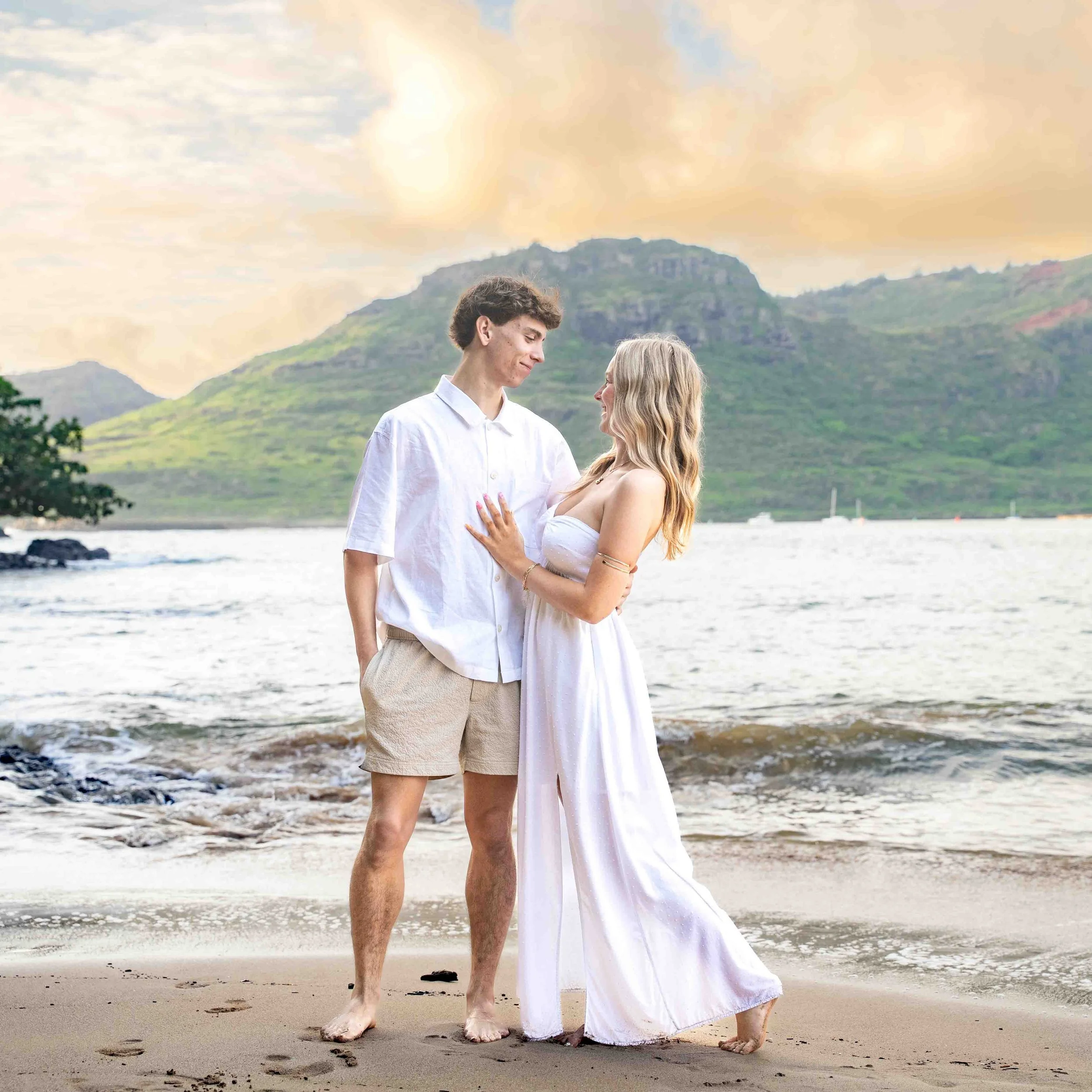 Young couple in white looking at each other on a Kauai beach.