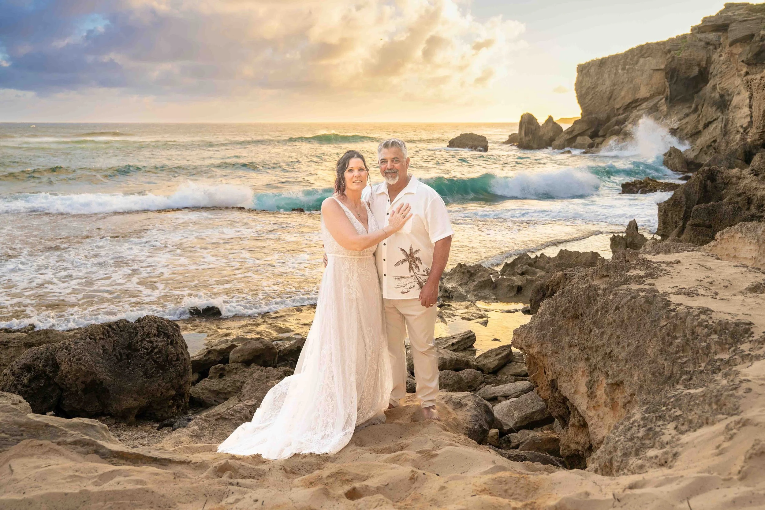 Older couple posing together on the rocky beach at Shipwreck Beach, Kauai, at sunset.