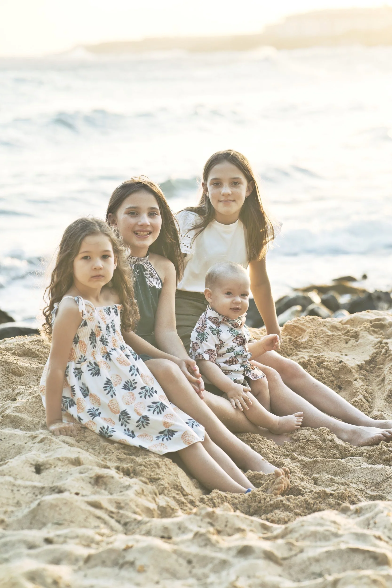 Four young siblings playing in the sand together on a Kauai beach.