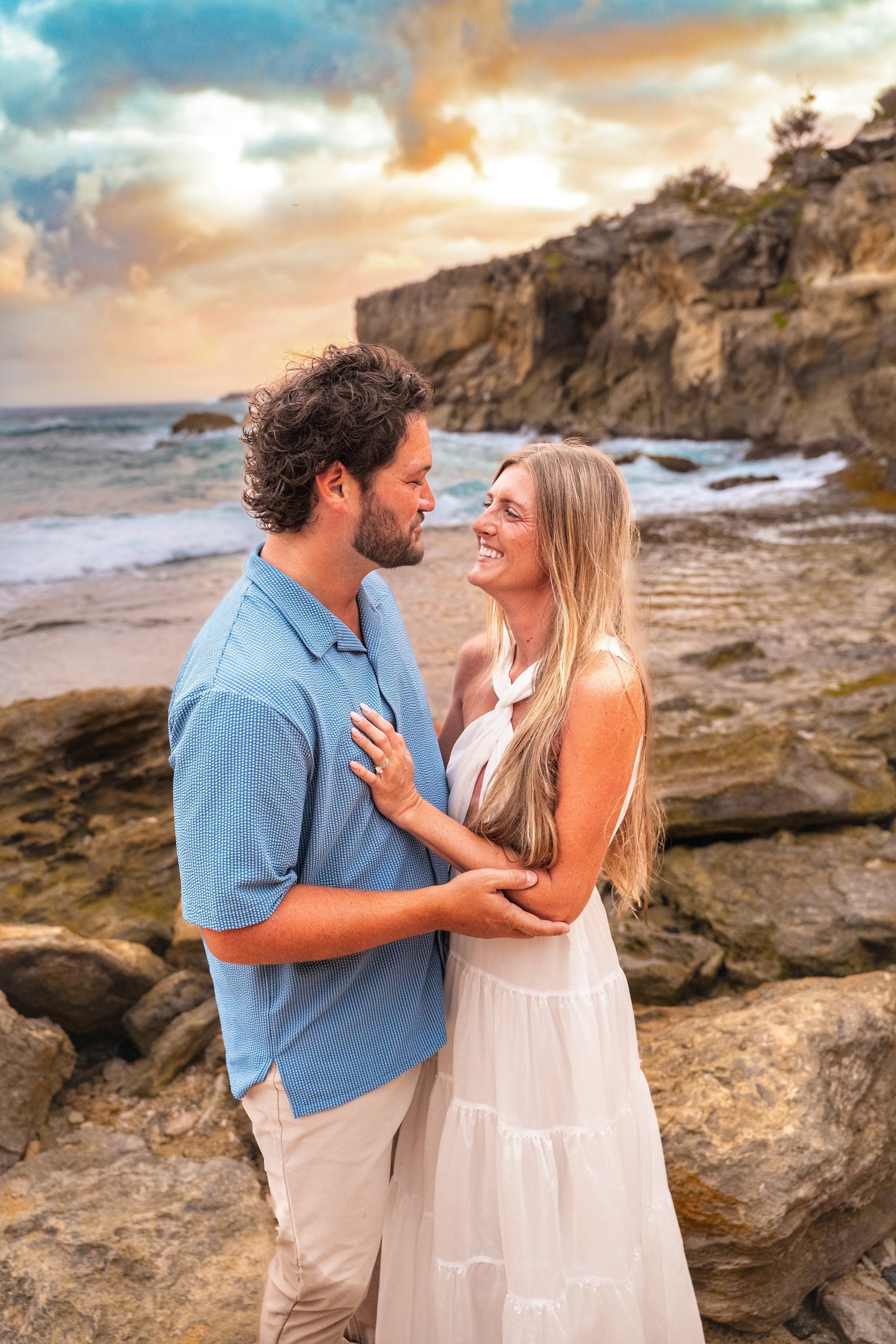 Smiling couple embracing on the rocky shore in golden light at Shipwreck Beach, Kauai.