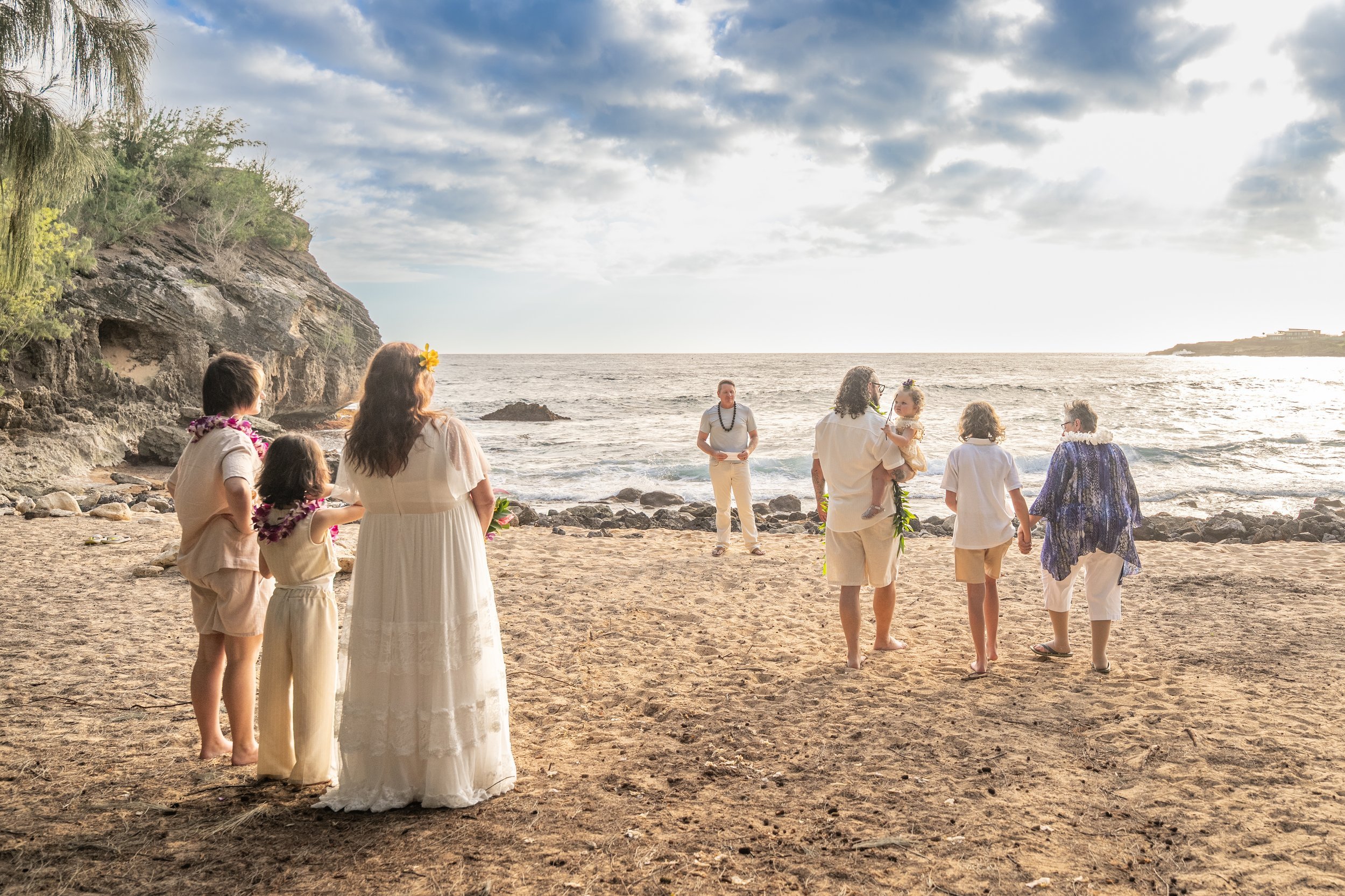 Wedding party standing on a Kauai beach looking out at the ocean.