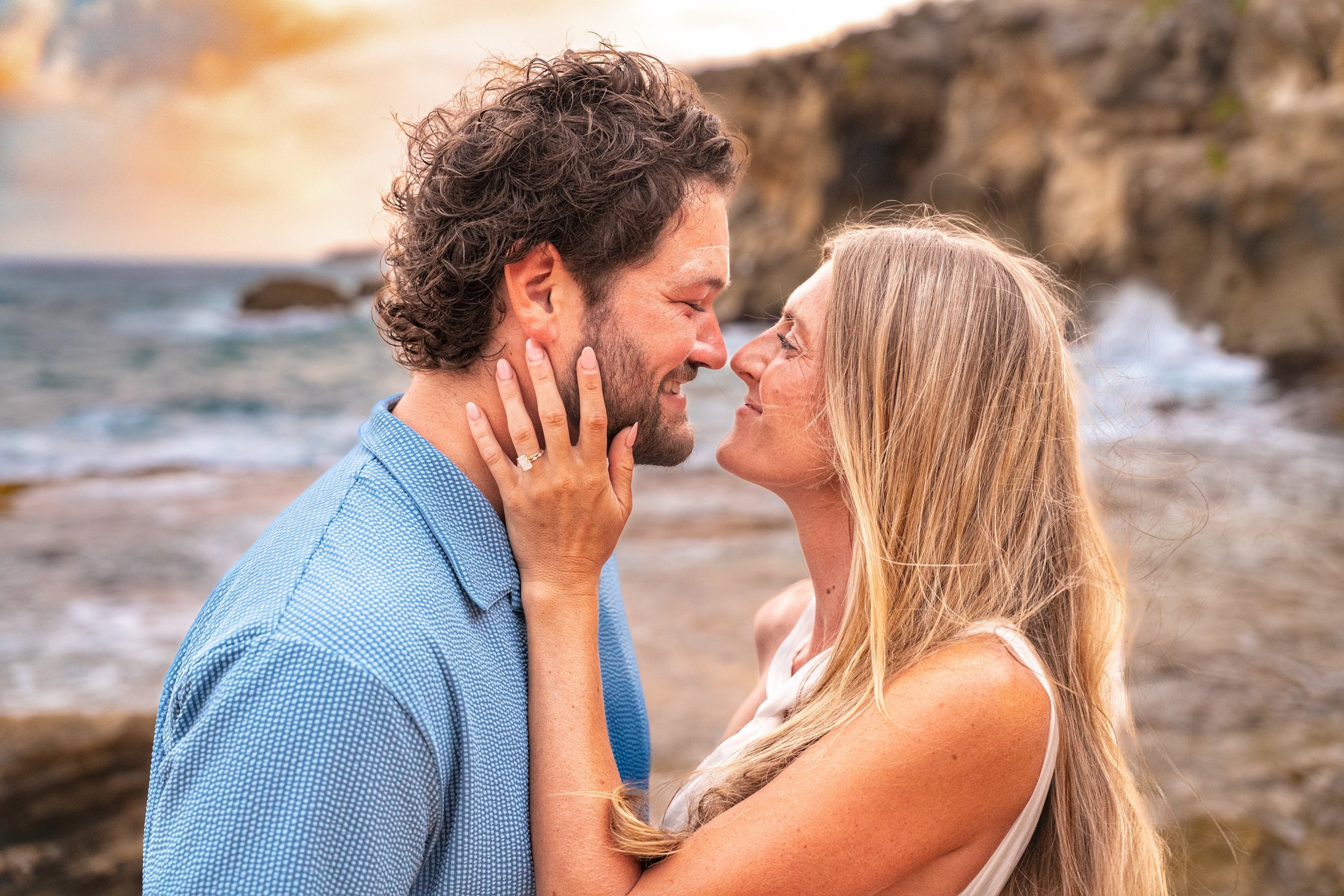 Newlywed couple sharing an intimate moment on a rocky Kauai beach at sunset.