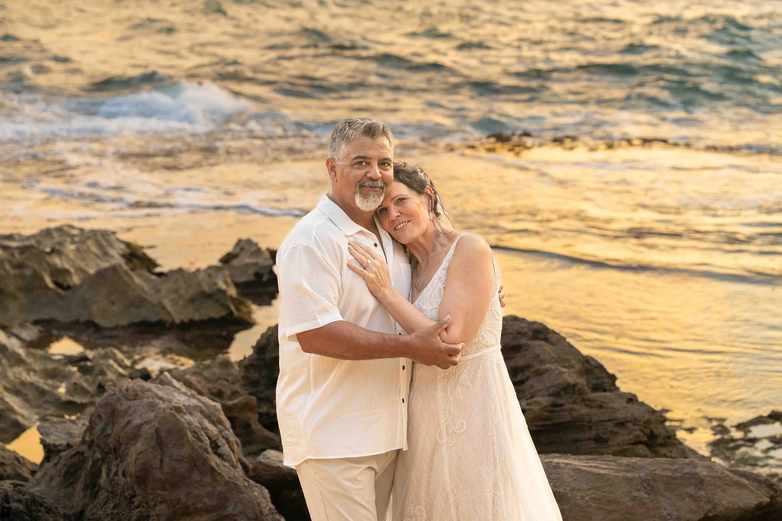Older couple embracing on the shore in golden light at Shipwreck Beach, Kauai.