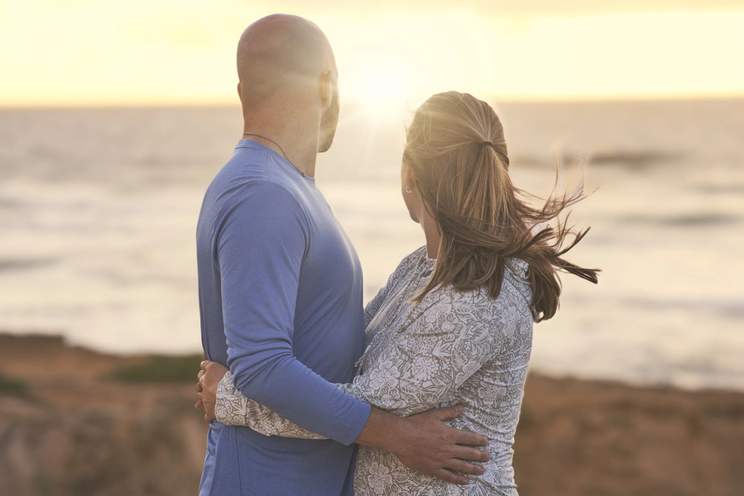 Couple embracing while watching the sunset over the ocean at Shipwreck Beach, Kauai.