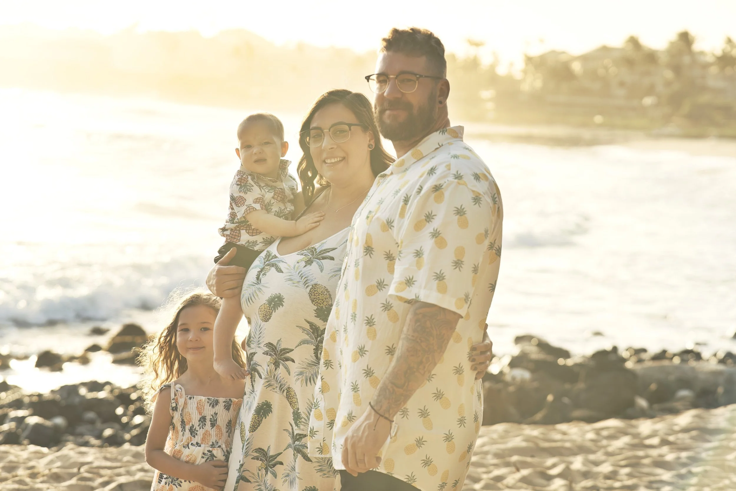 Family of four standing close together on a Kauai beach in golden sunset light.