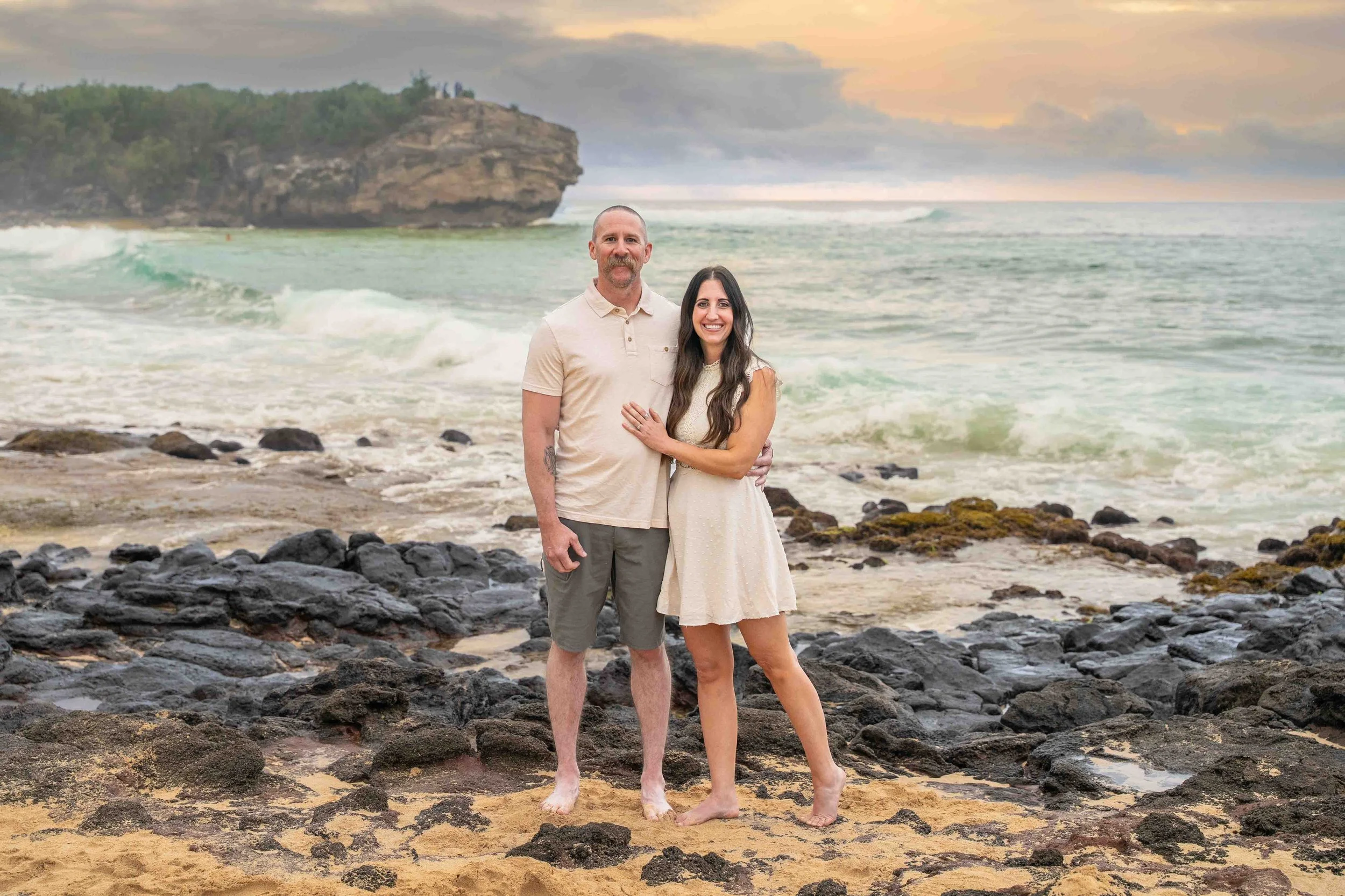 Couple posing on the beach with a sea stack behind them at Shipwreck Beach, Kauai.