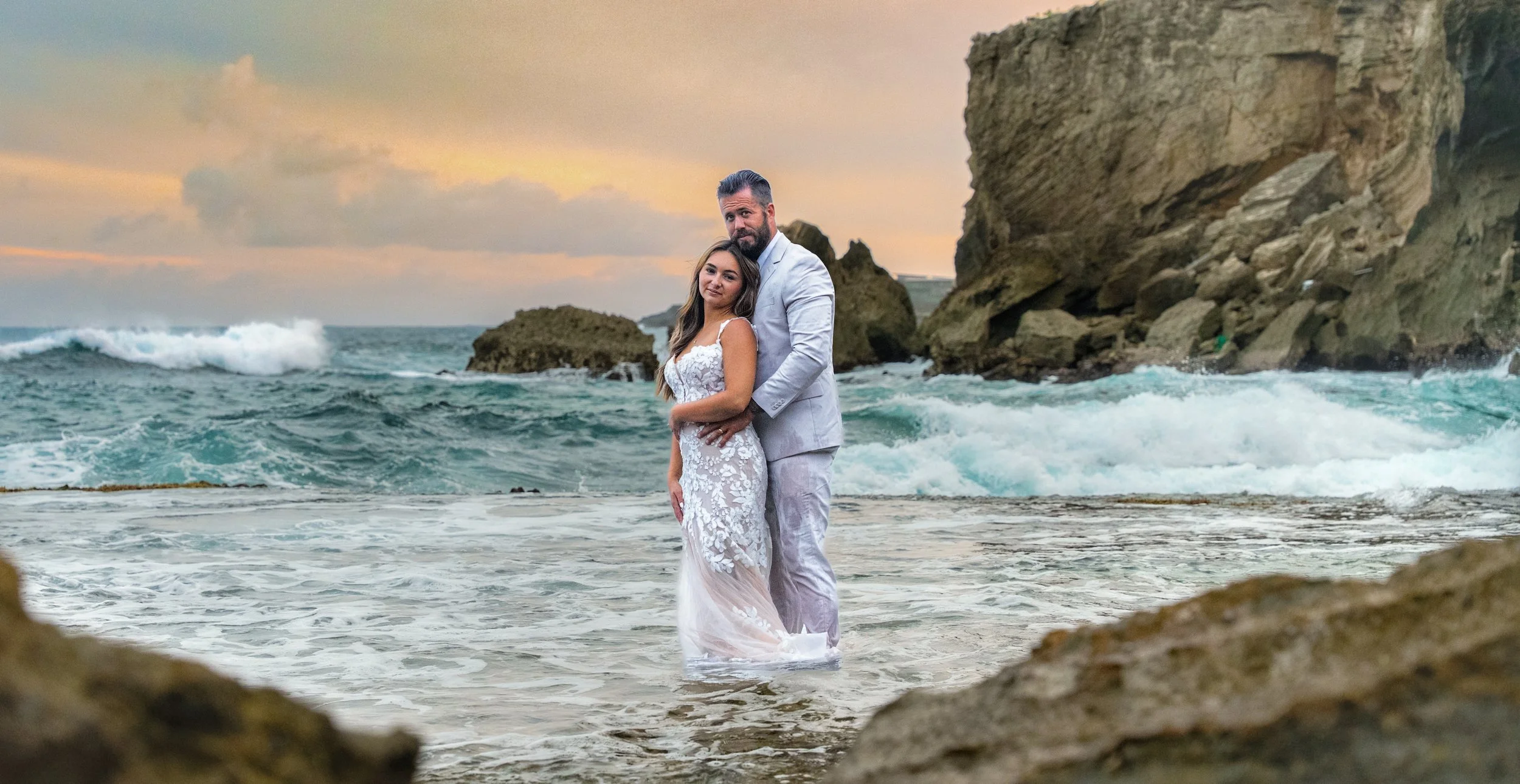 Newlywed couple embracing in the shallow surf at Shipwreck Beach, Kauai.