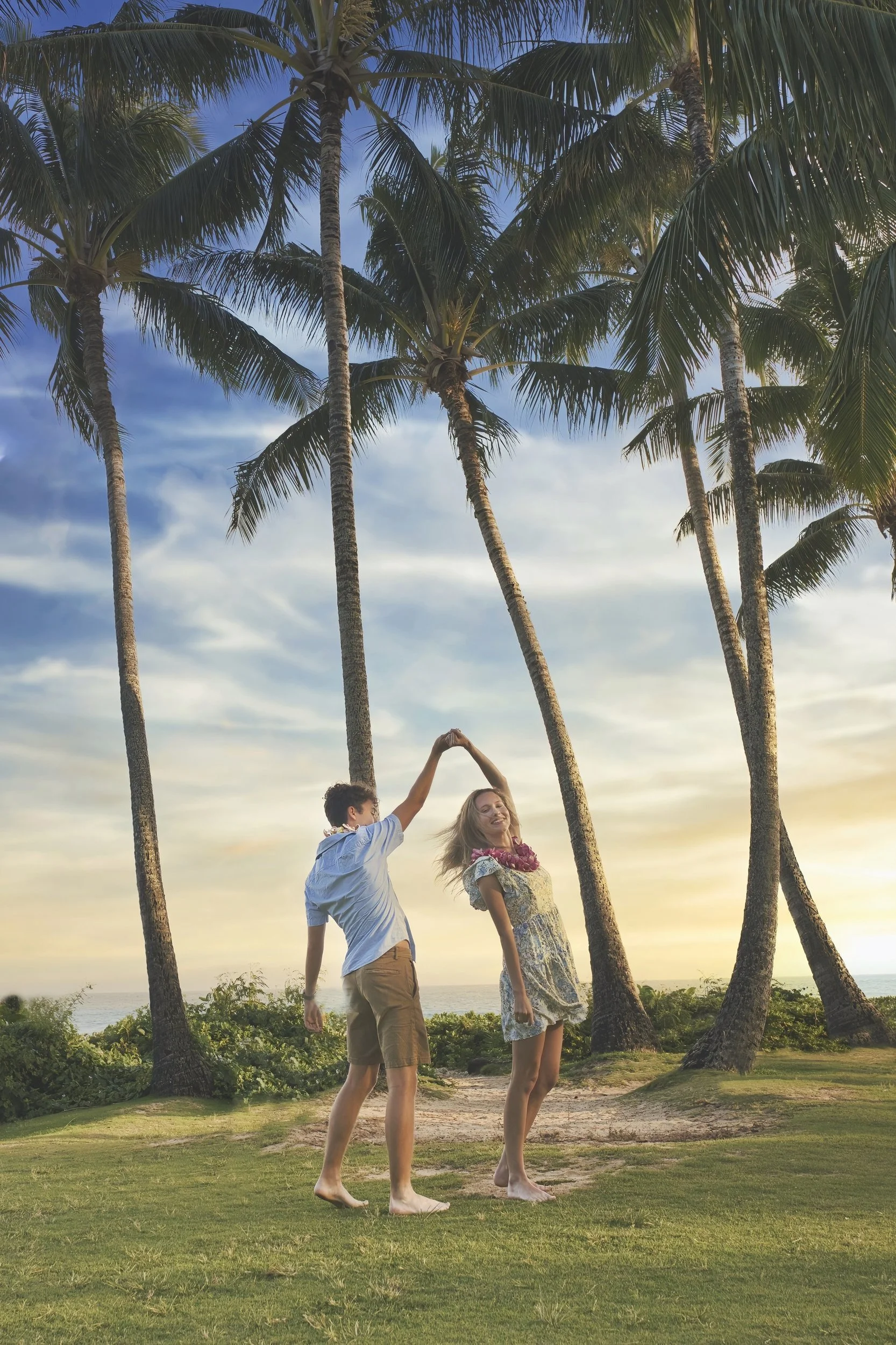 Couple dancing together under tall palm trees in Kauai at sunset.