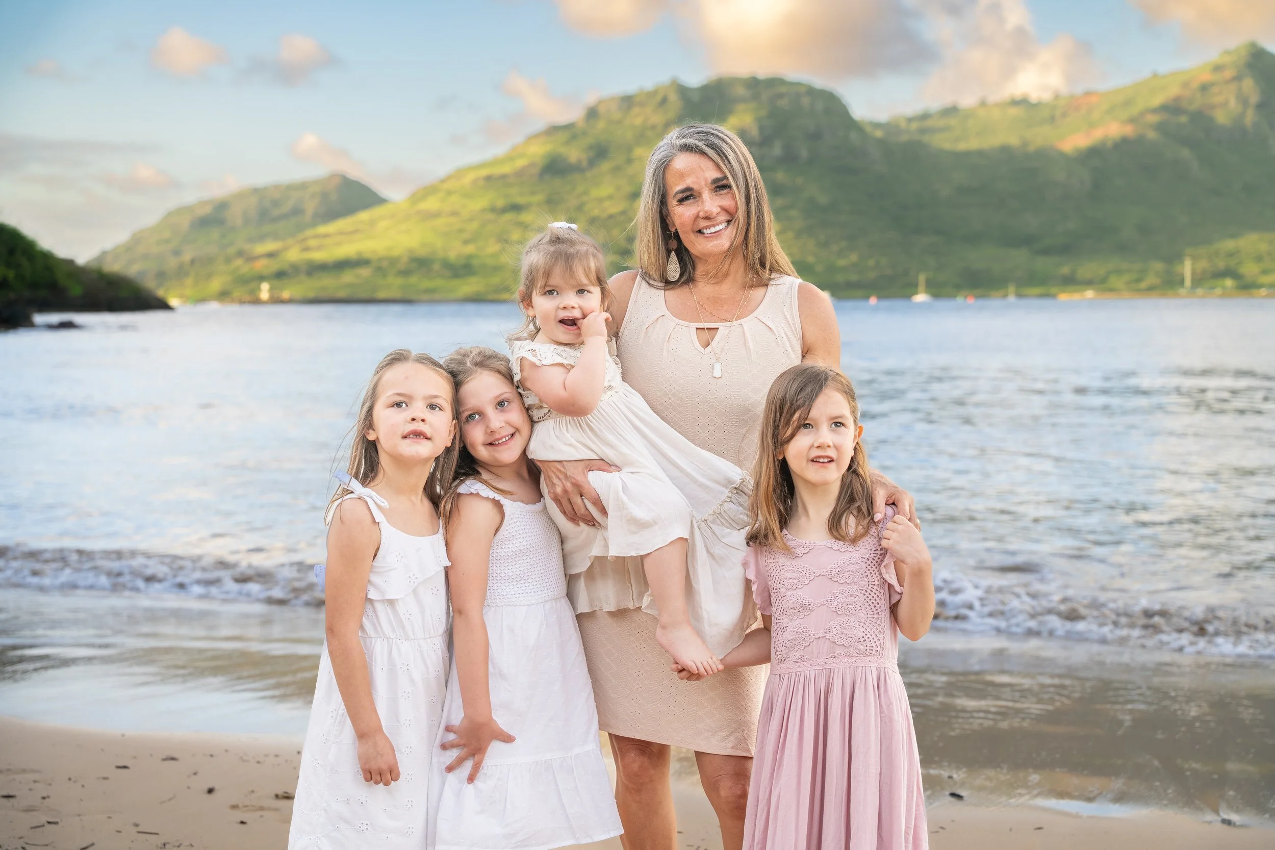 Grandmother posing with her four granddaughters on a Kauai beach at golden hour.