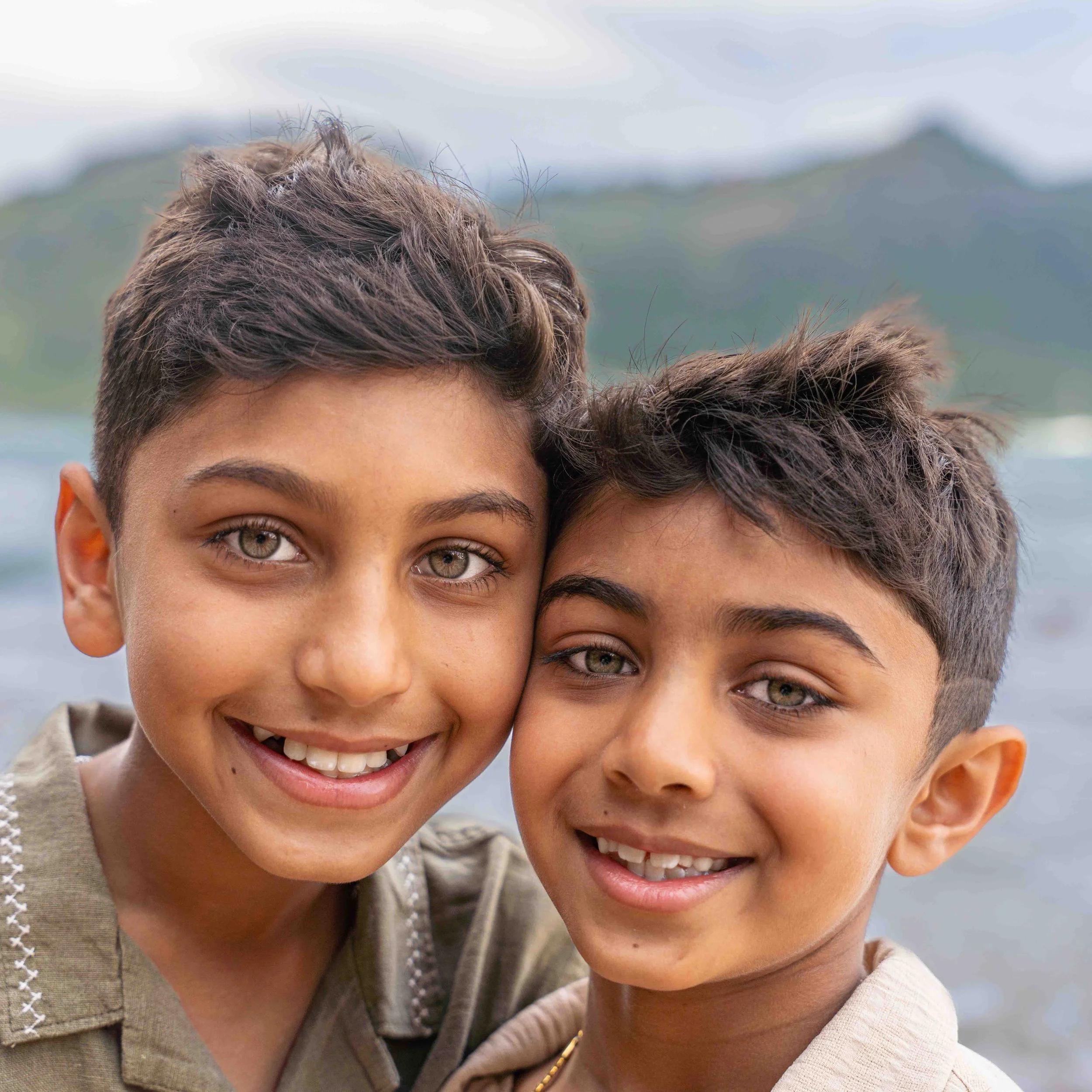 Two young brothers smiling with their heads together on a Kauai beach.