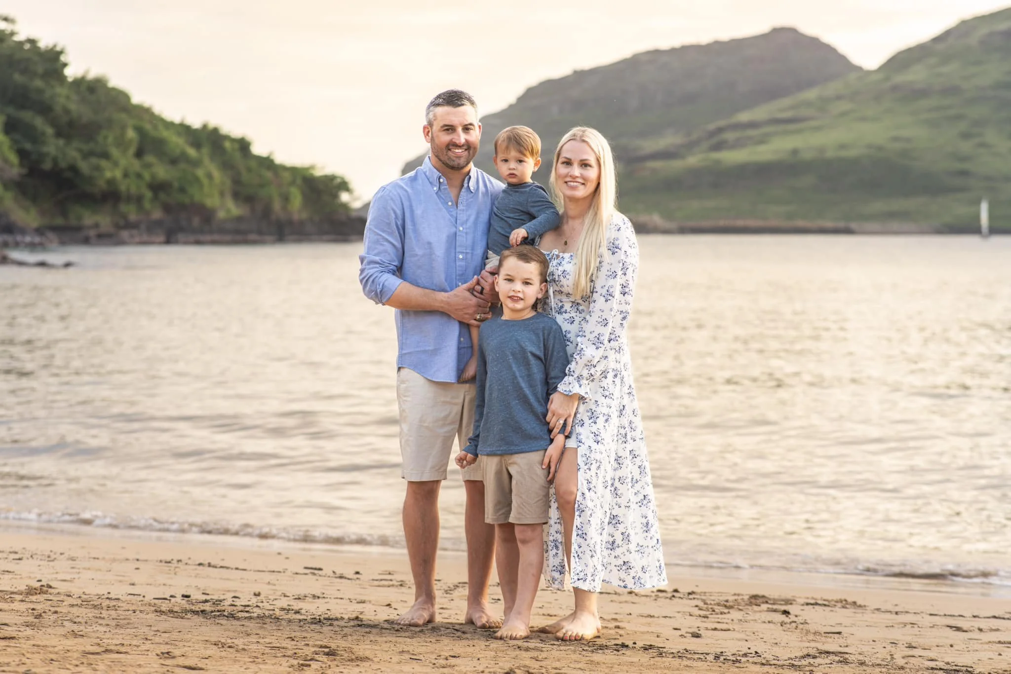 Family of four poses at golden hour on a Kauai beach with a mountain rising behind them.