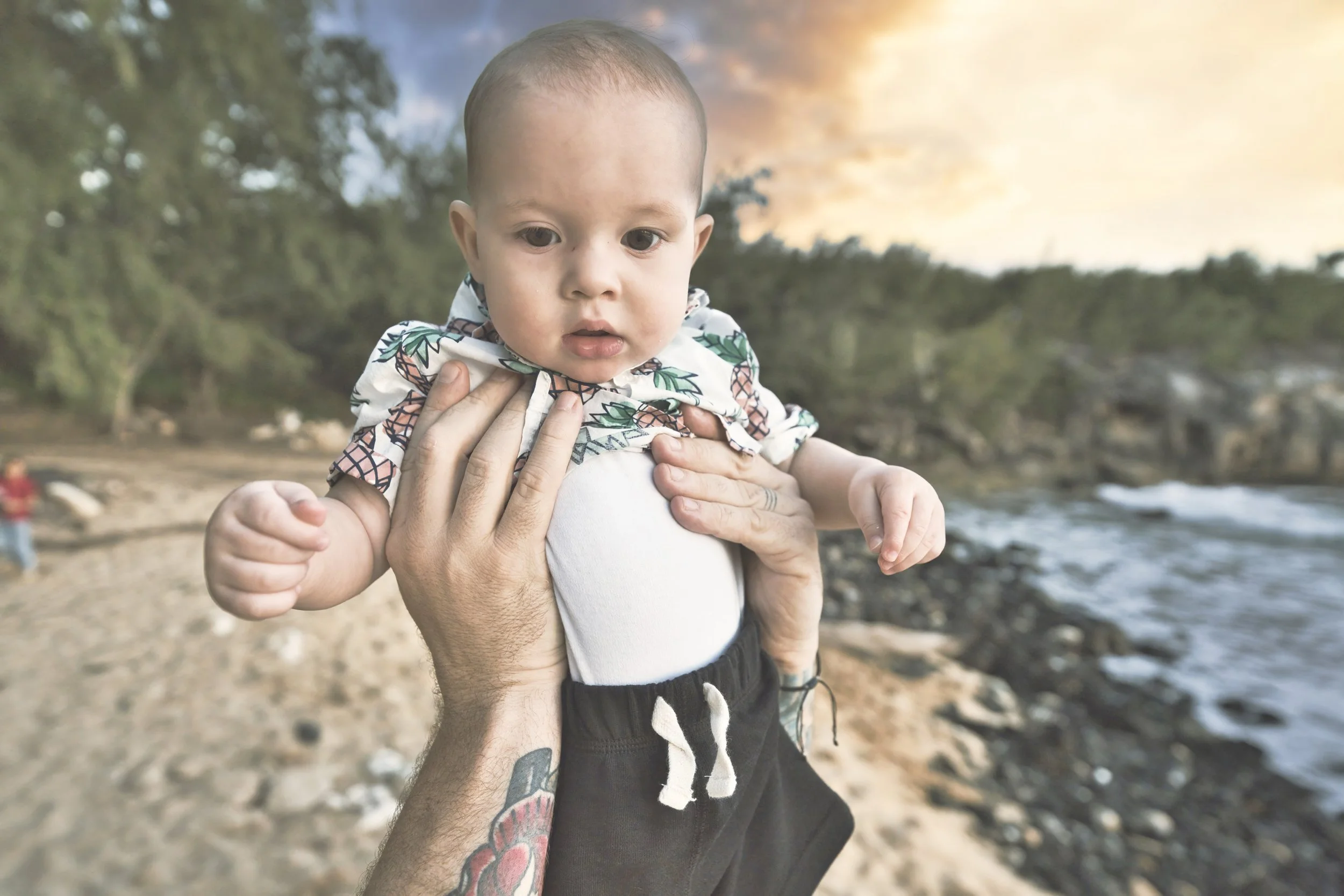 Dad lifting his baby toward the camera on a Kauai beach at sunset.