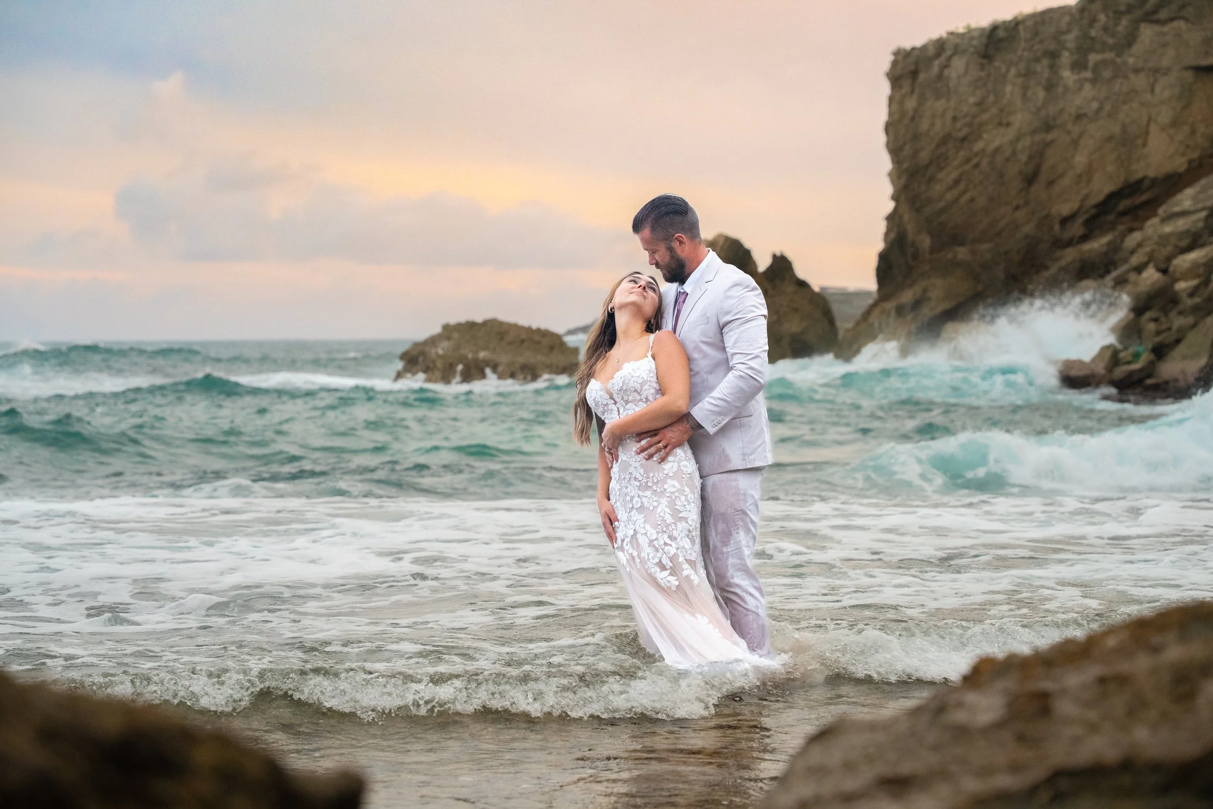 Newlywed couple standing in the ocean surf at sunset at Shipwreck Beach, Kauai.