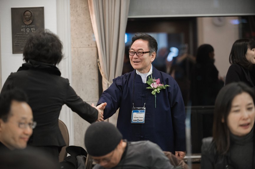 Andrew Zhang, dressed in navy blue, is shaking hands with a woman at the SVA Alumni Association.