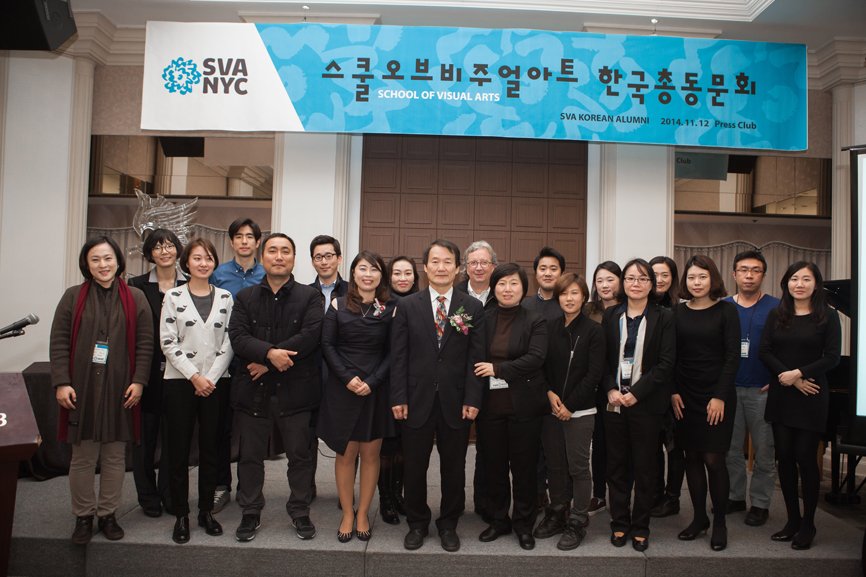 A group photo of 19 individuals taken beneath the alumni gathering banner.